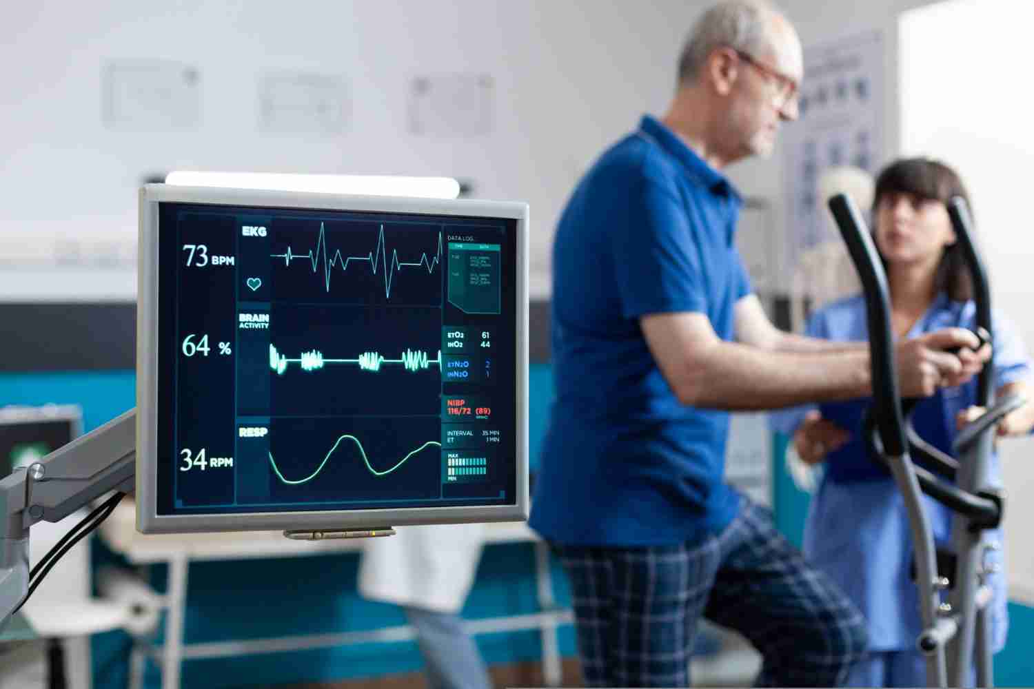 A hospital monitor showing vital signs, with a patient unconscious in the background.
