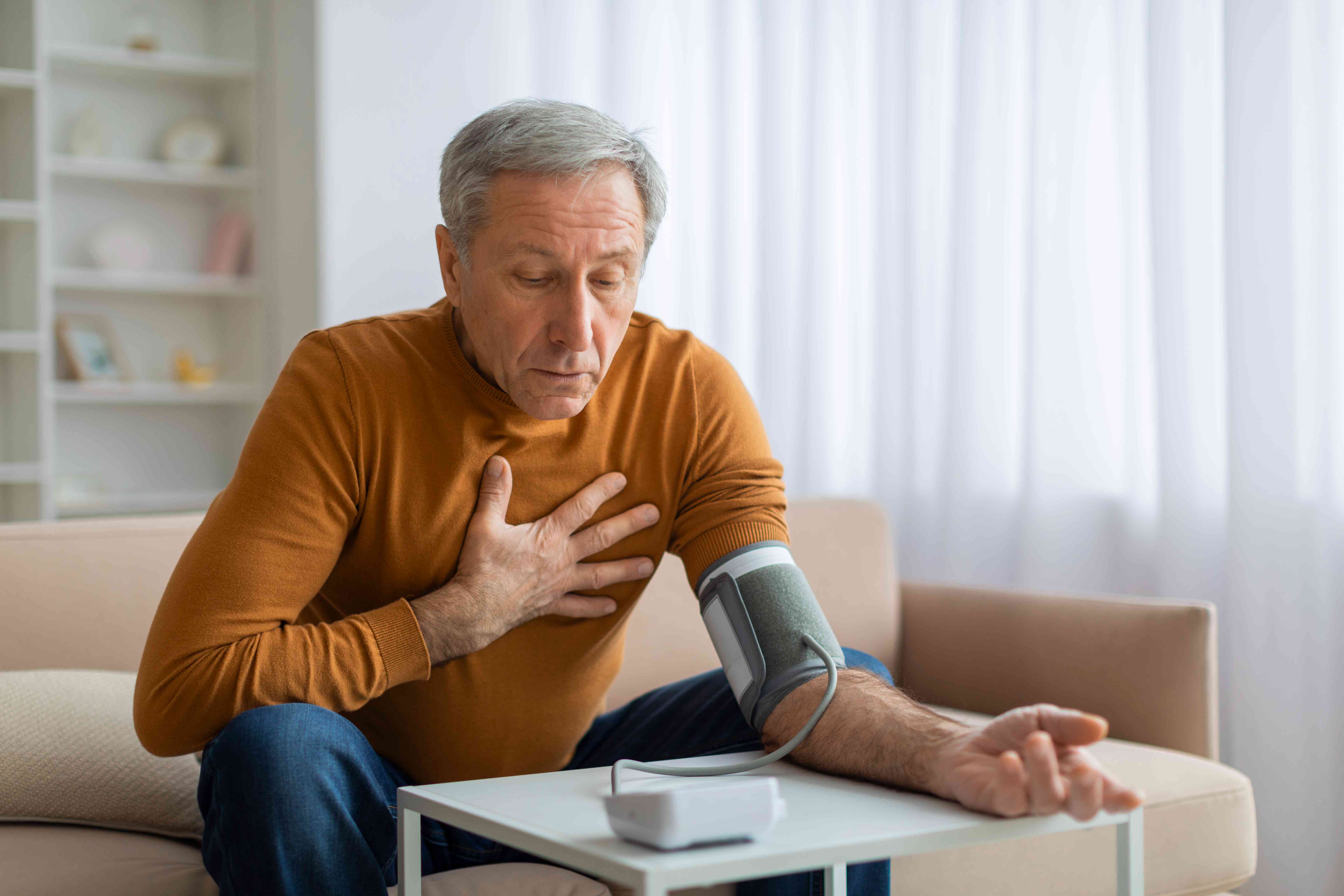 **Elderly man checking his blood pressure at home while holding his chest.