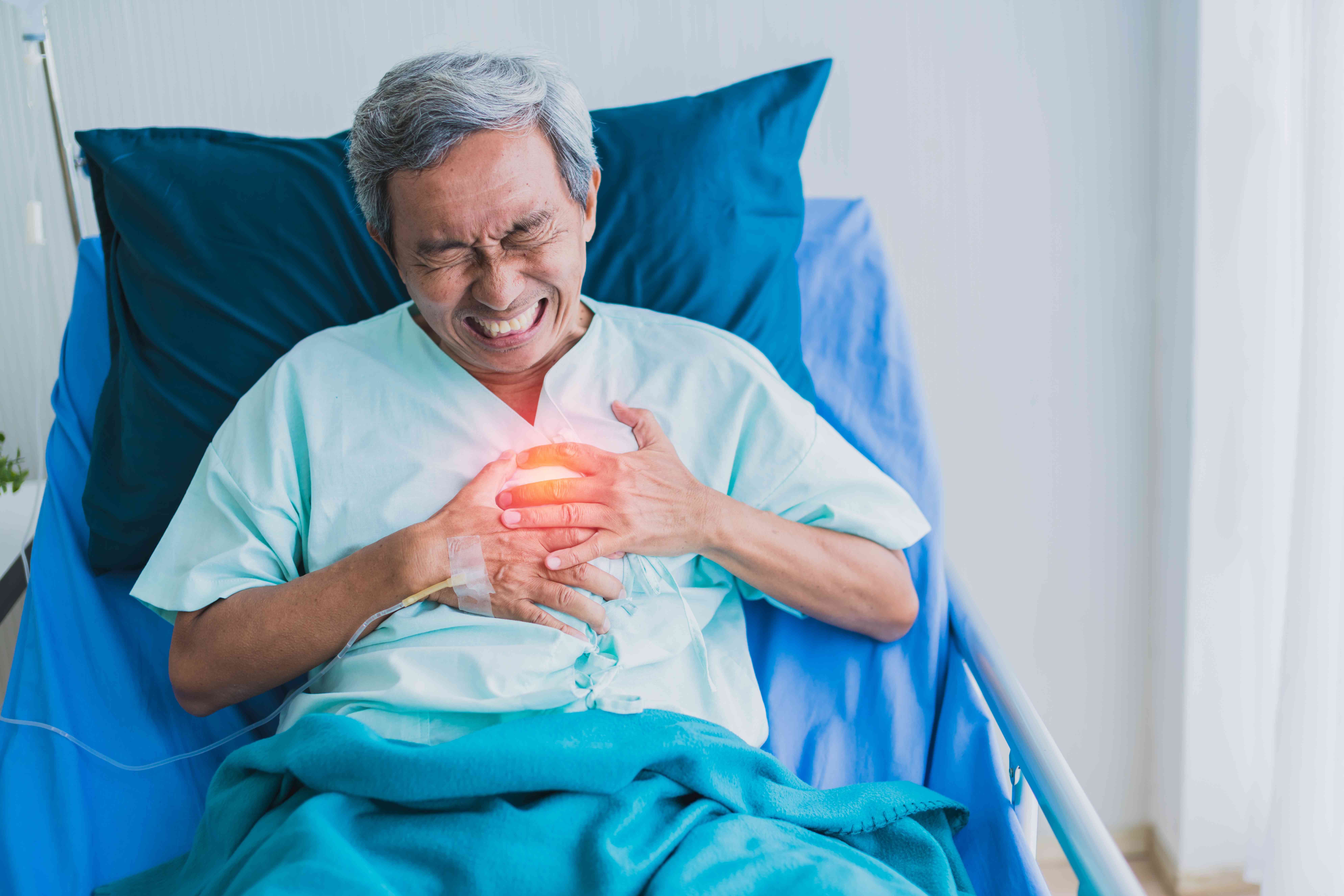 Elderly man in hospital bed, clutching his chest in severe pain.