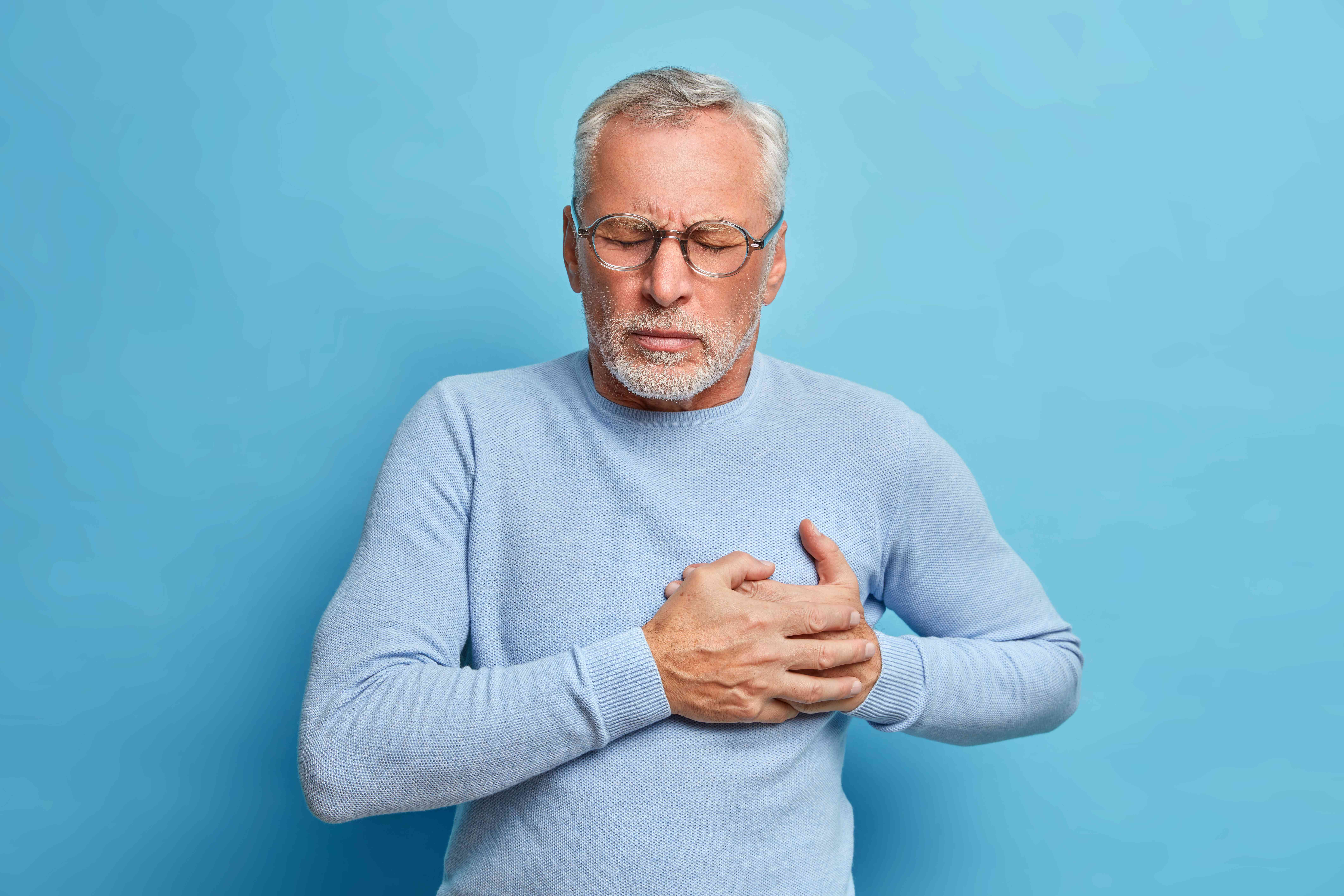 Senior man holding his chest with eyes closed, looking uncomfortable.