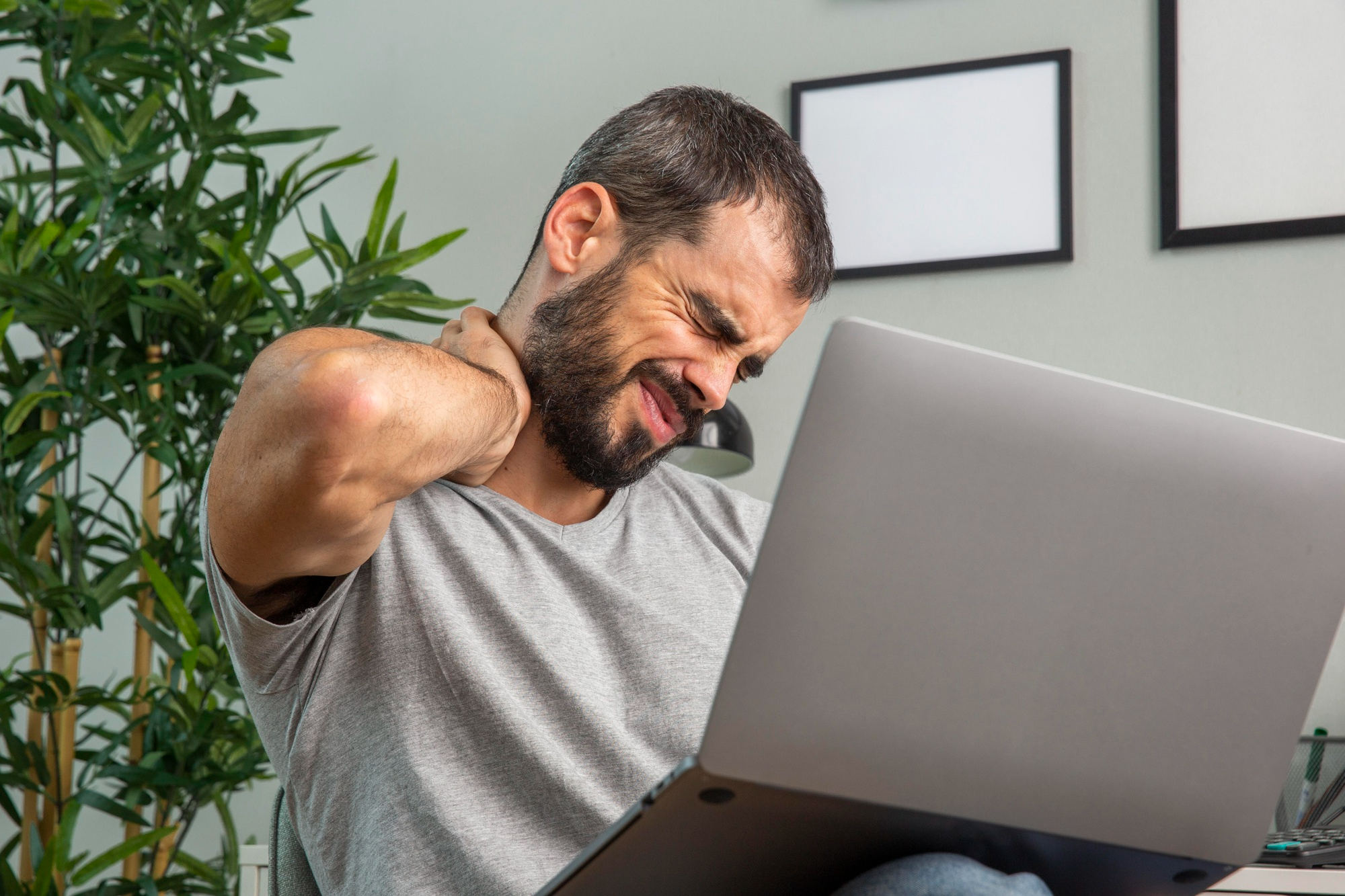 A young man experiencing neck pain from prolonged laptop use due to poor posture.