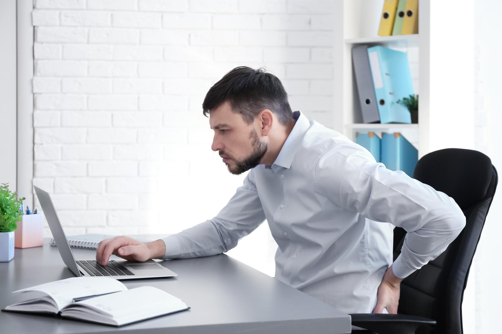 A man sitting at his desk with his neck and shoulders slouched forward, demonstrating poor posture that can lead to neck and joint pain over time.