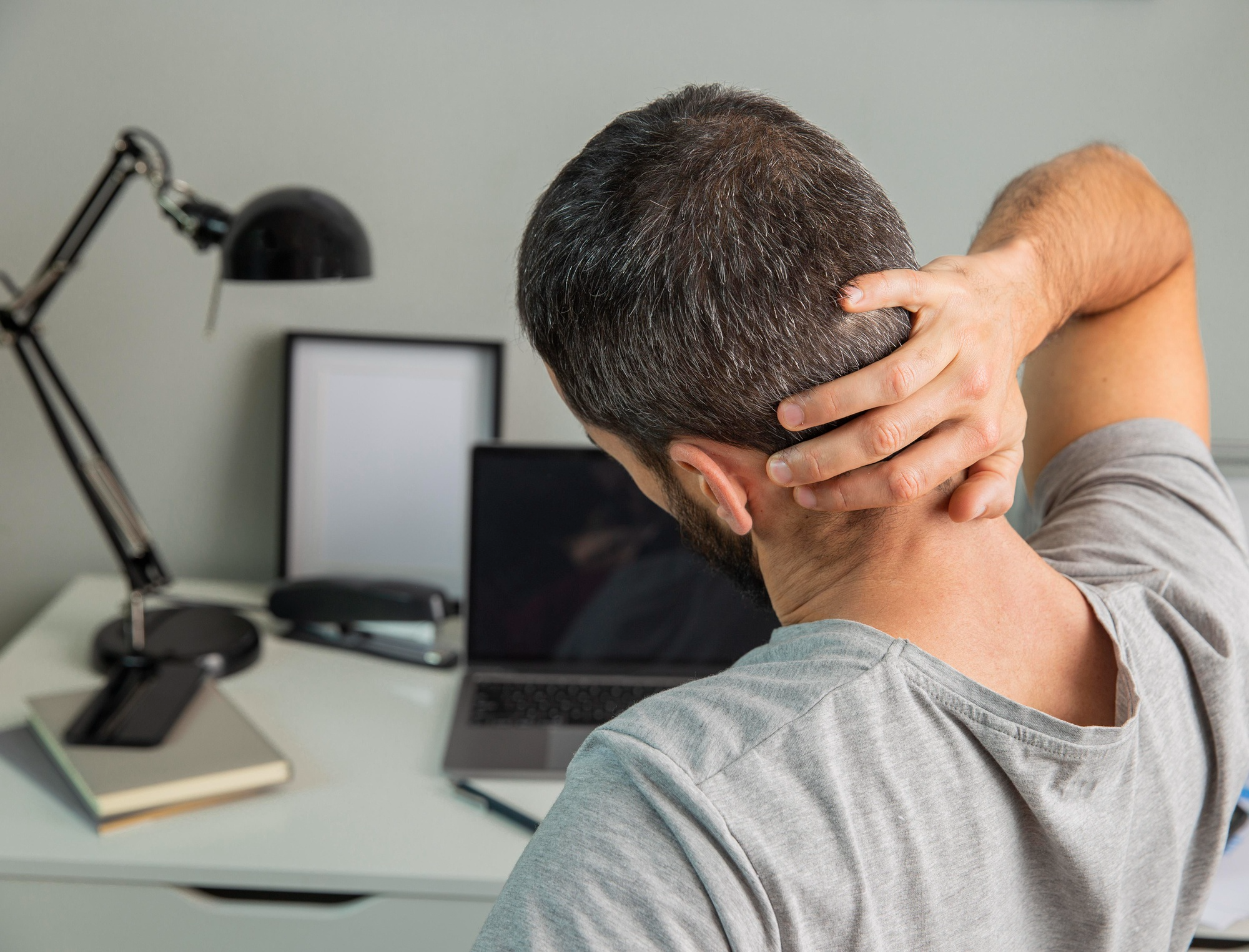 A young man experiences neck stiffness from prolonged laptop use leading to muscle strain or cervical spine tension that may need orthopedic attention.
