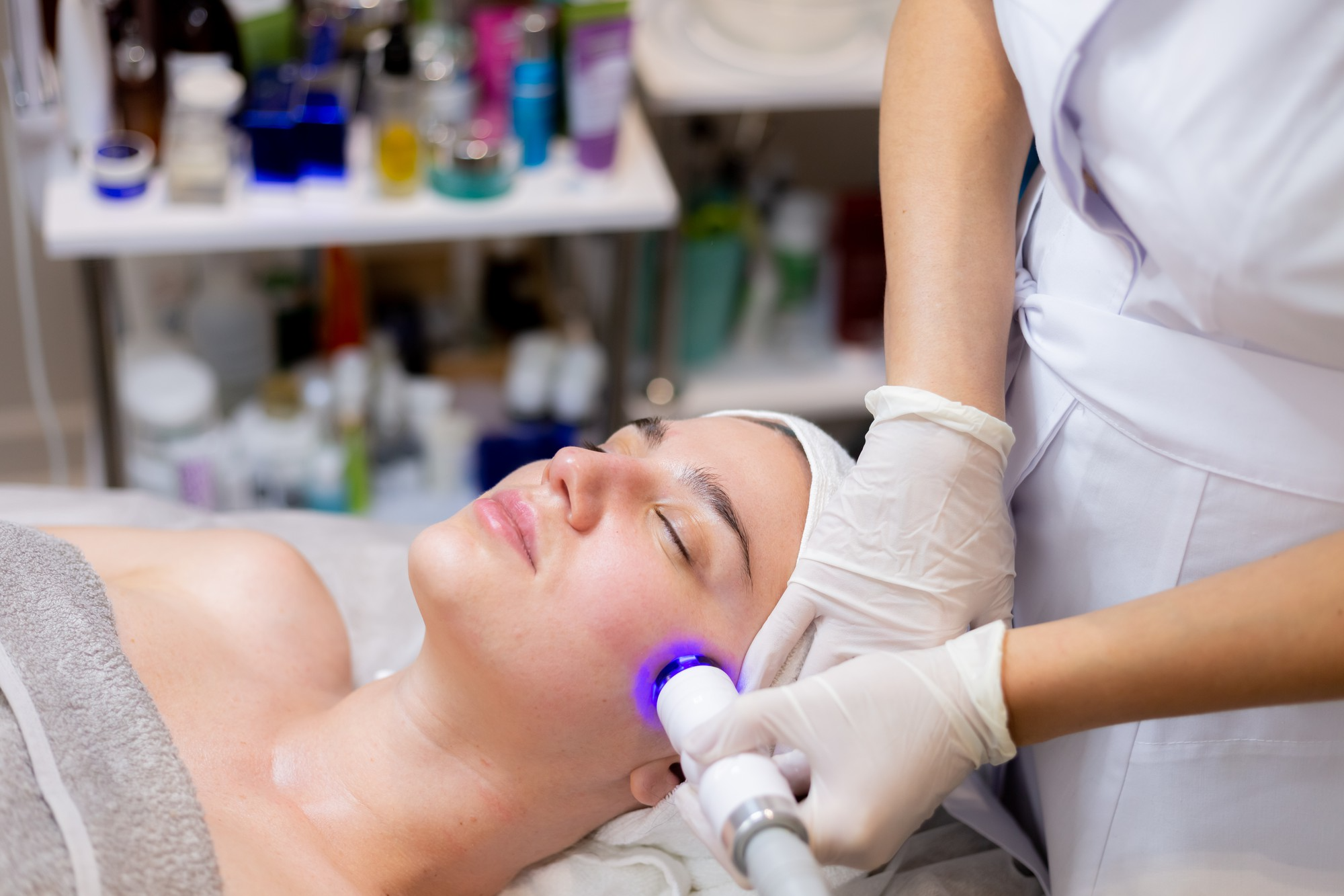 A woman at a dermatologist receiving LED light therapy facial treatment for glowing skin.