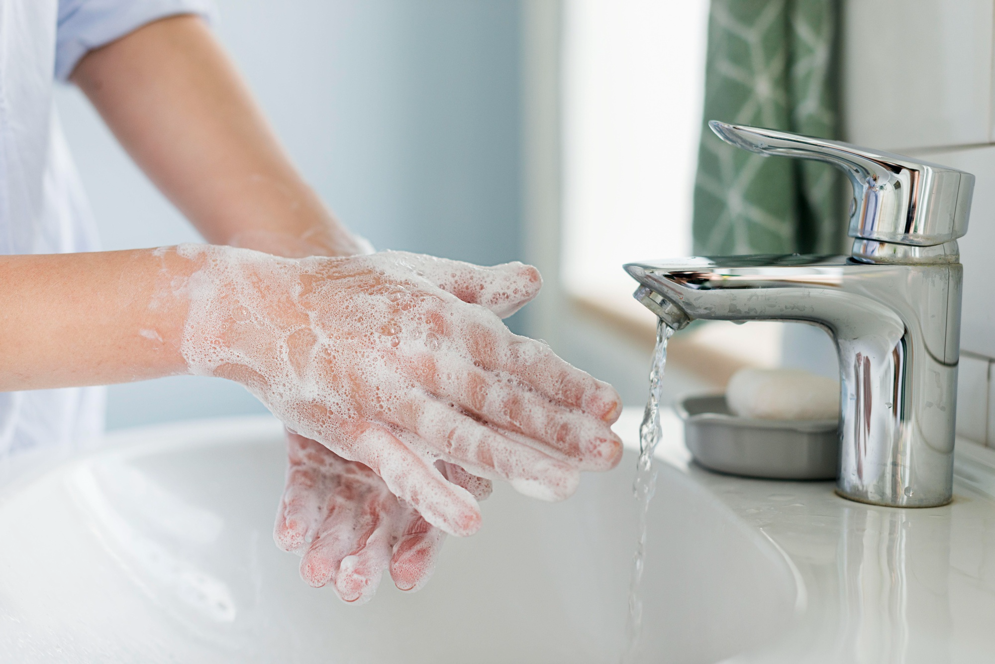 A child whose hands are lathered with soap, water running from the tap of a sink and a bar of soap kept next to it.