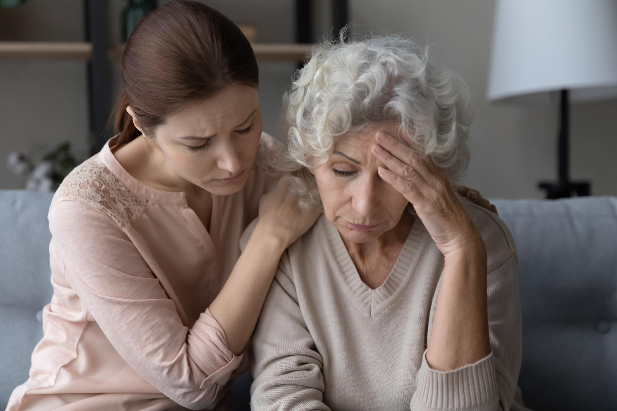 A young woman supporting her elderly mother who has Alzheimer’s and looks troubled and disturbed.