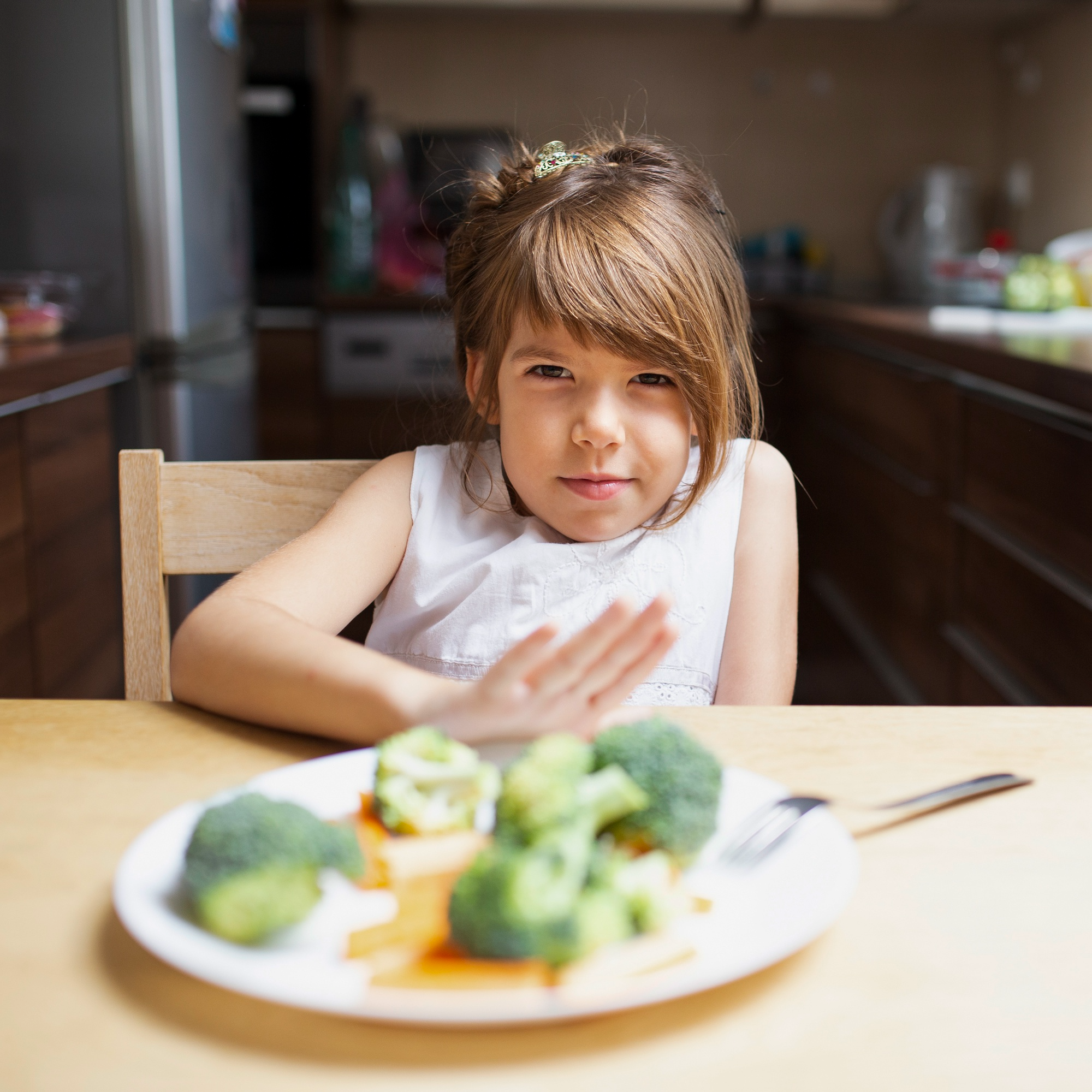 A girl who is a picky eater refusing a plate of healthy food filled with vegetables, reflecting common challenges parents face in encouraging healthy eating habits for kids.