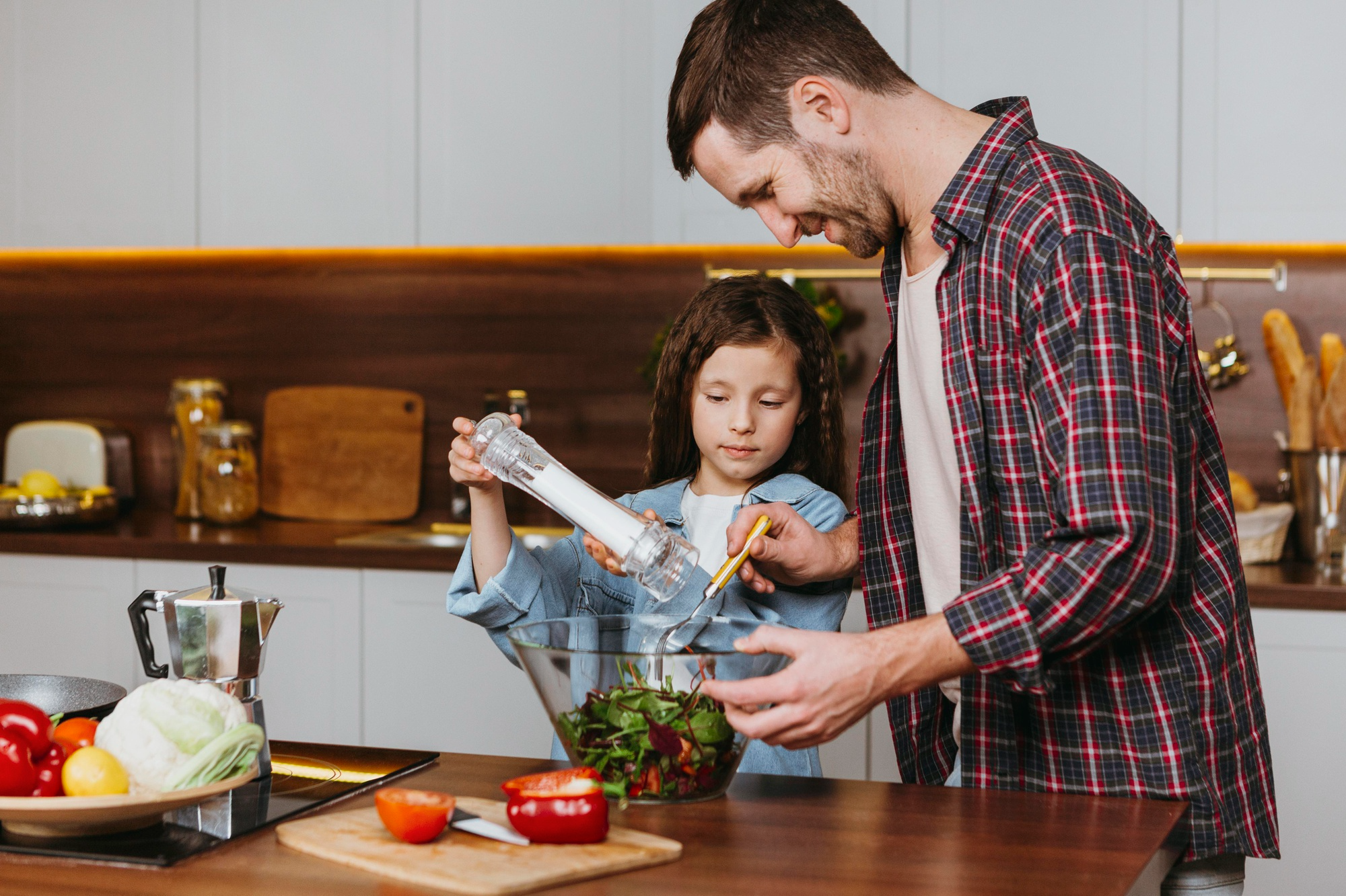 A child helping a parent in the kitchen to prepare a healthy meal with fresh vegetables and ingredients.