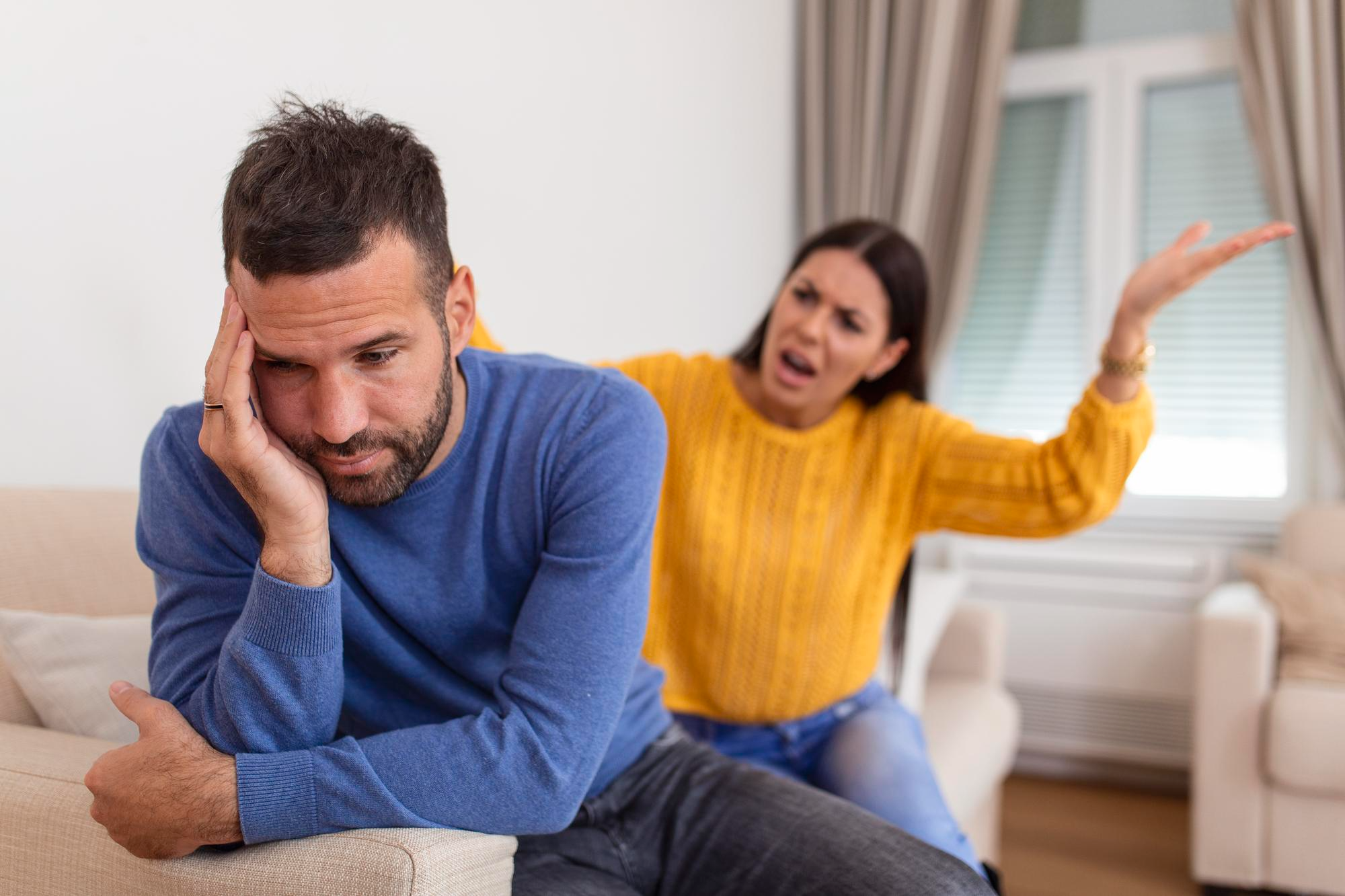 A couple sitting on a sofa and arguing, representing relationship conflicts and emotional disturbance.