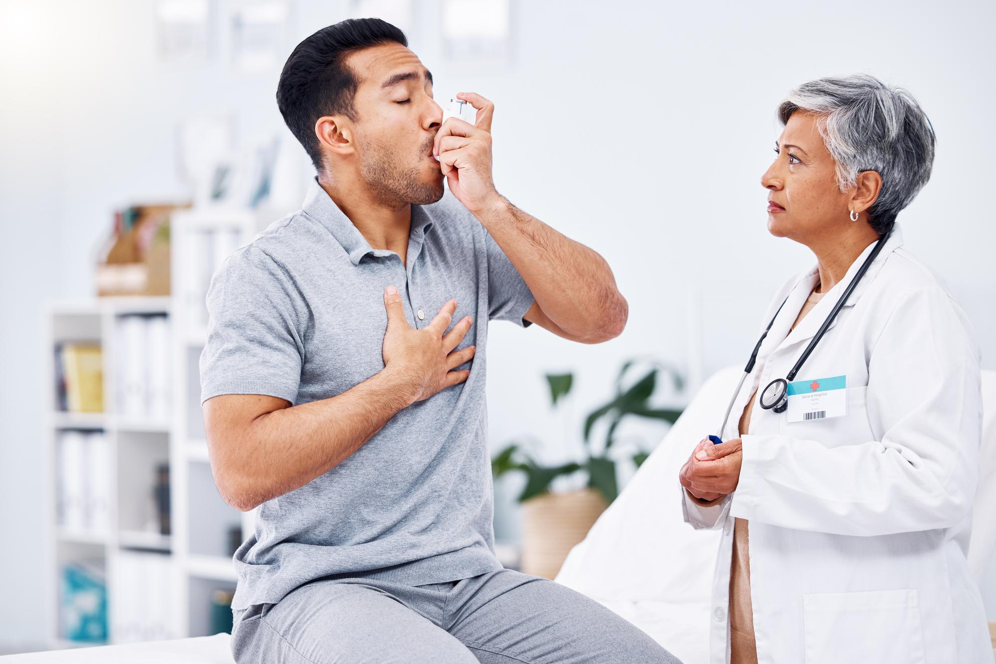 An image showing a man taking an asthma inhaler while a doctor observes, representing medical care for breathing difficulties.