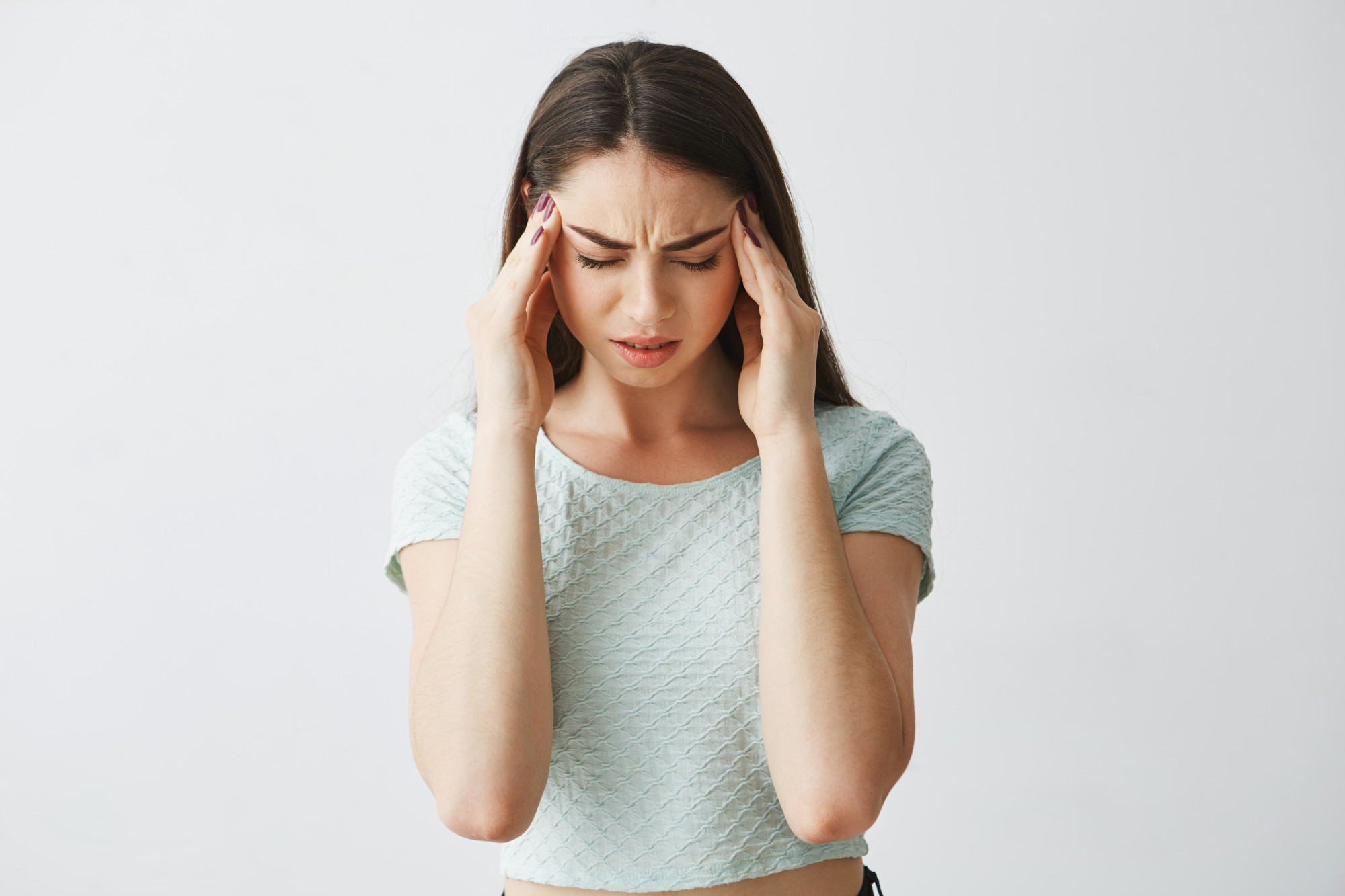 A woman is pressing her temples with her eyes closed, expressing intense discomfort and sensitivity, representing the throbbing head pain commonly associated with migraines.