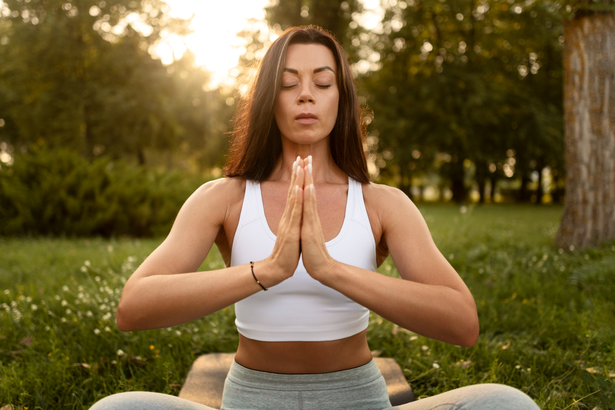 A calm woman sitting in a meditative pose surrounded by nature, representing relaxation techniques used to reduce PMS cramps, stress and mood swings.