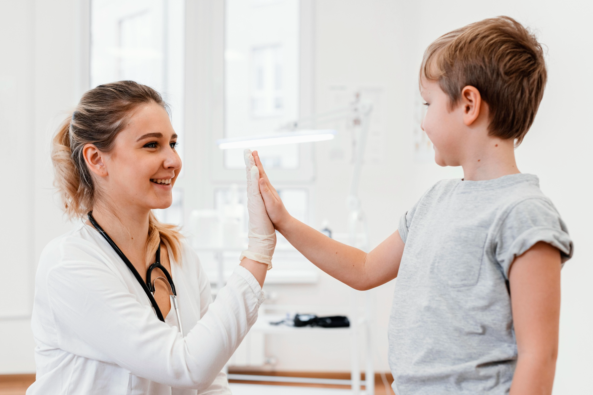 A smiling child raises their hand to high-five a friendly doctor in a clinical setting.