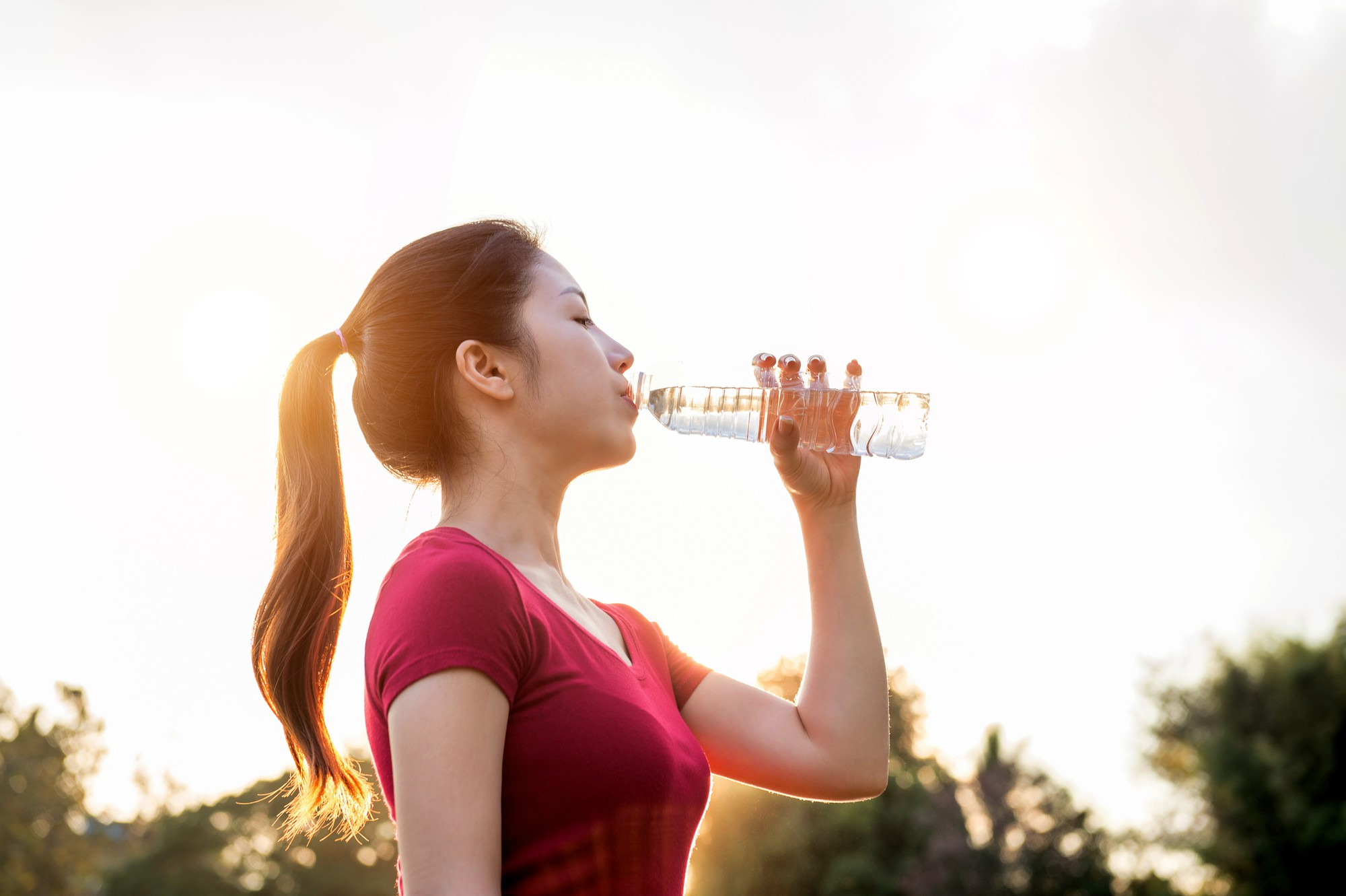 A woman holds a bottle and takes a sip of water, appearing refreshed and relaxed.