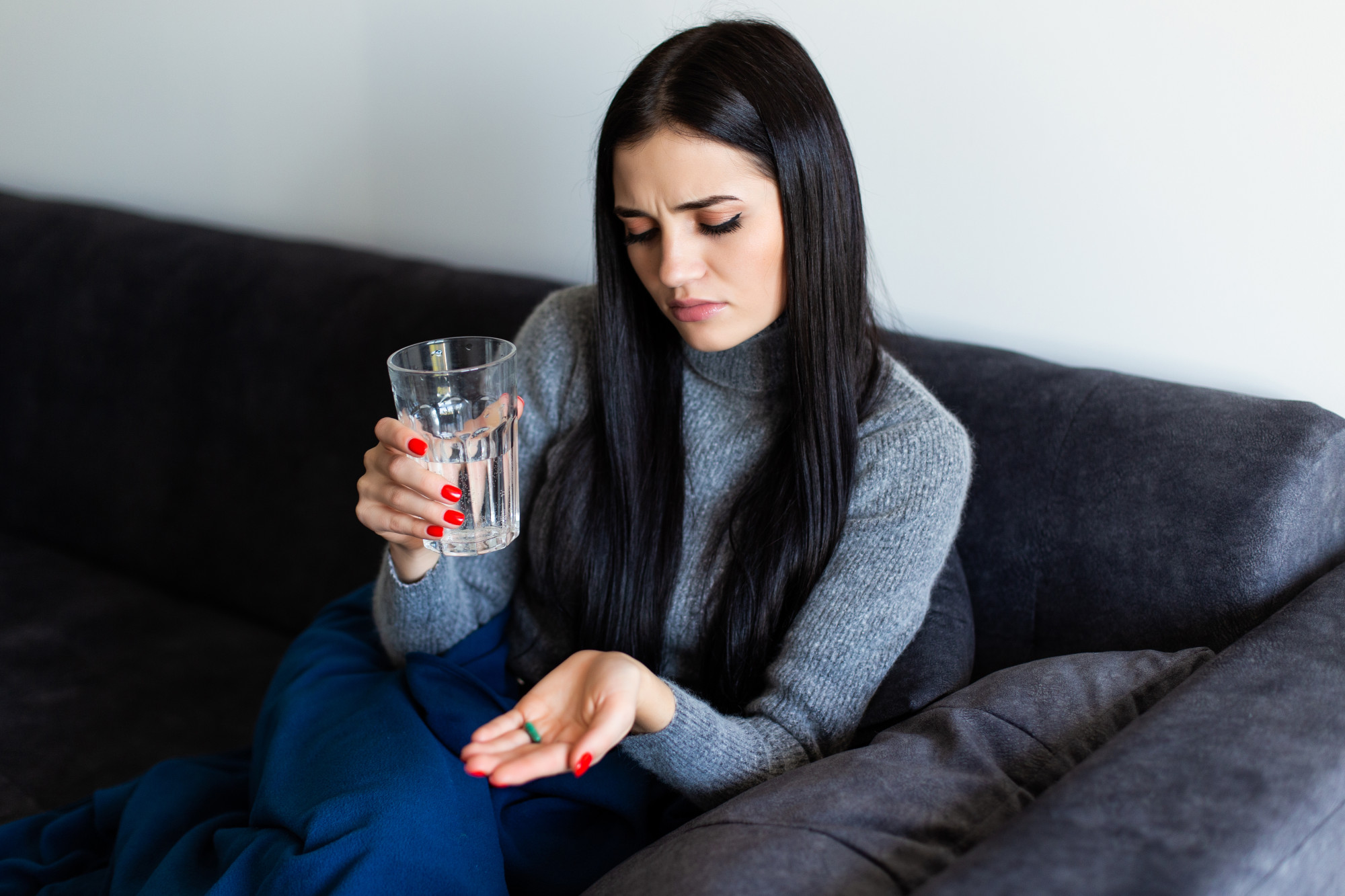 A woman holding painkillers with a thoughtful or uncertain expression.