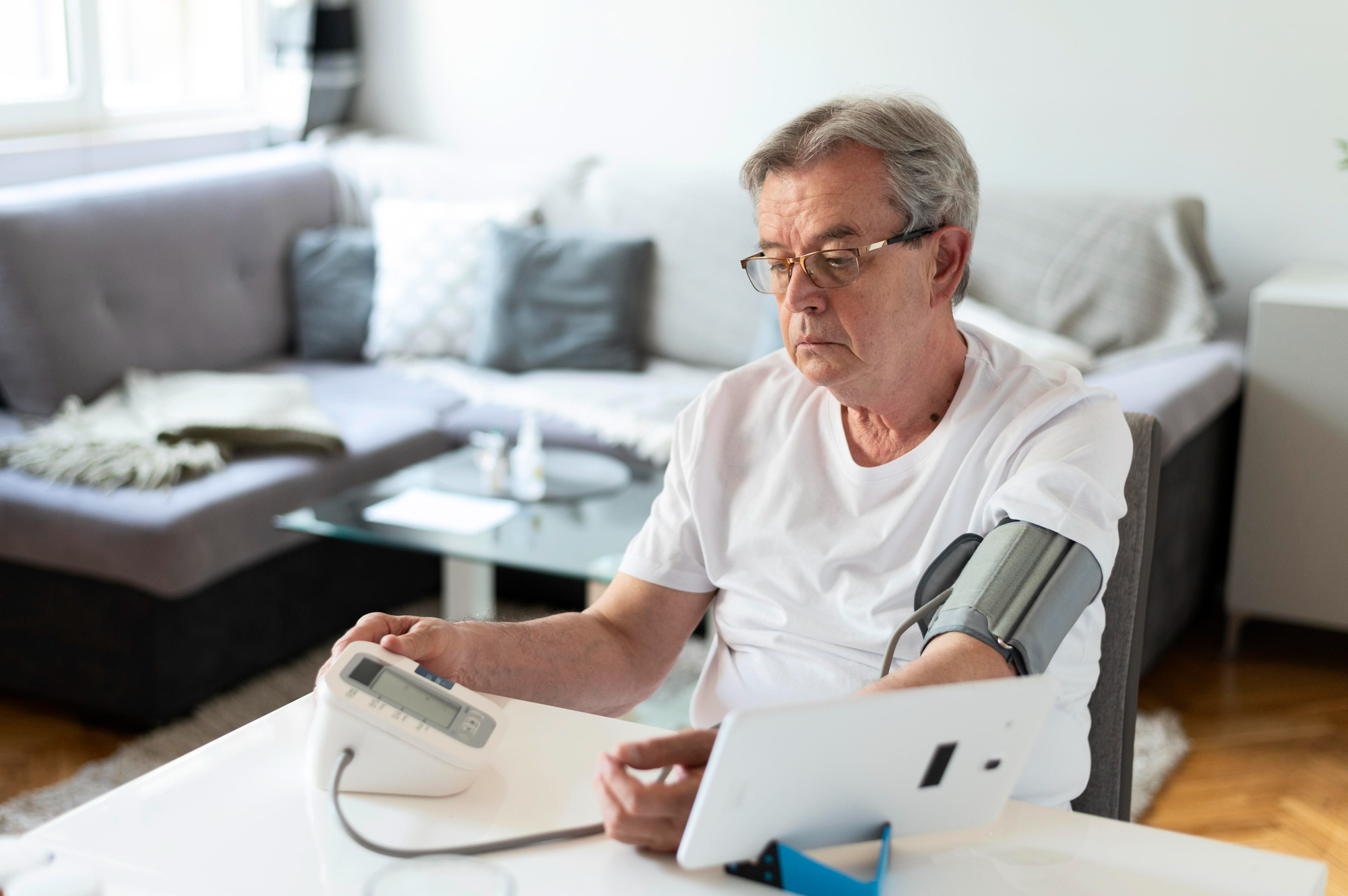 An elderly man sits calmly while measuring his blood pressure using a digital BP monitor.