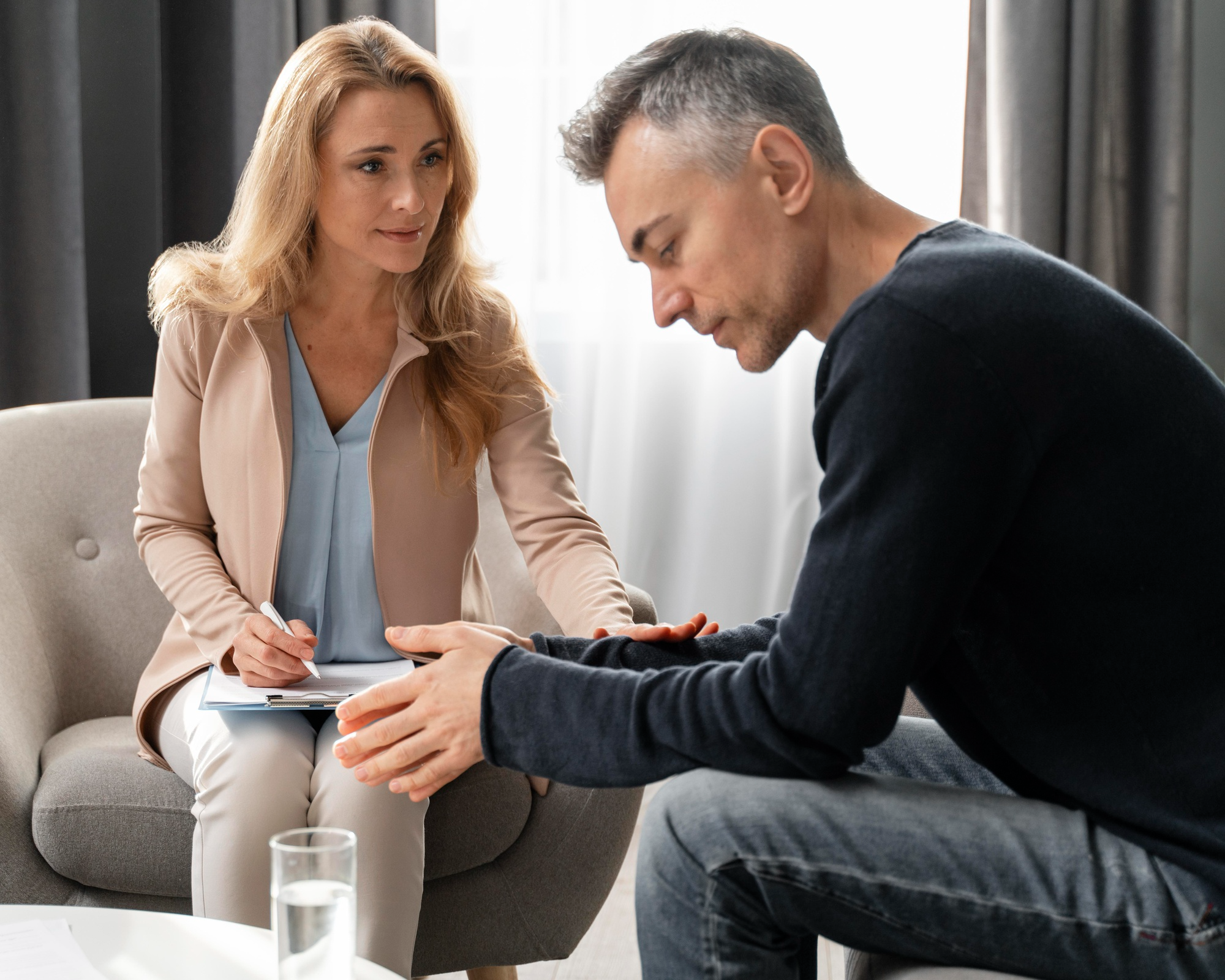 A man sits in a therapy session speaking with a mental health professional in a calm, supportive environment.