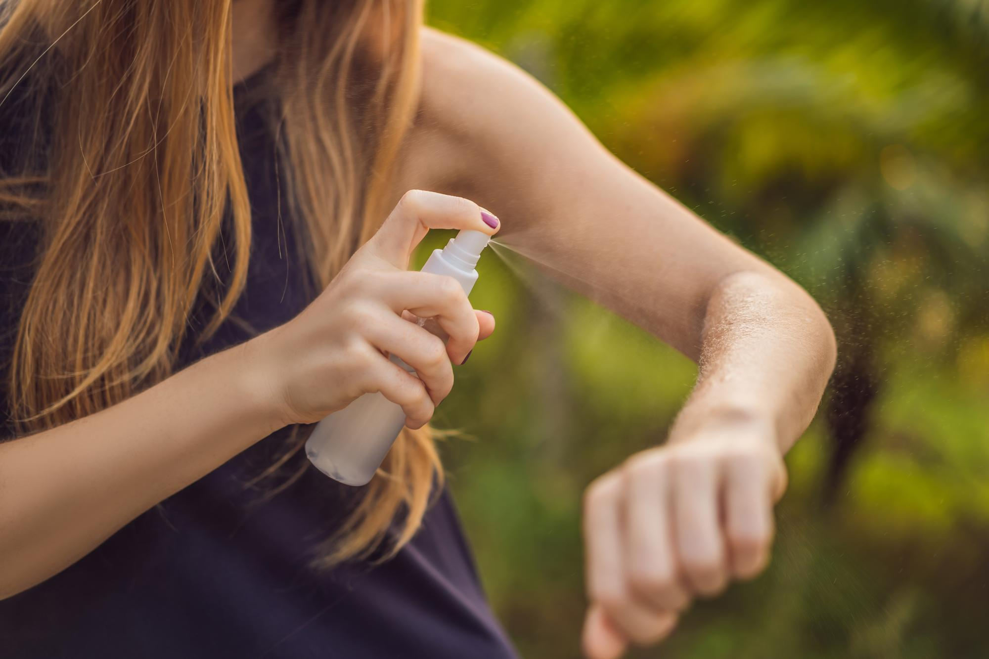 A woman spraying mosquito repellent on her skin, highlighting an effective preventive measure against mosquito bites and dengue infection.
