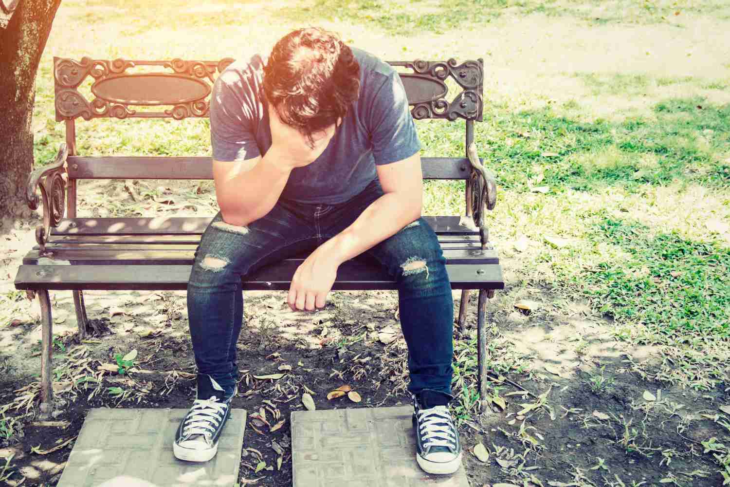  A man resting on a park bench, drenched in sweat, holding his head and looking fatigued