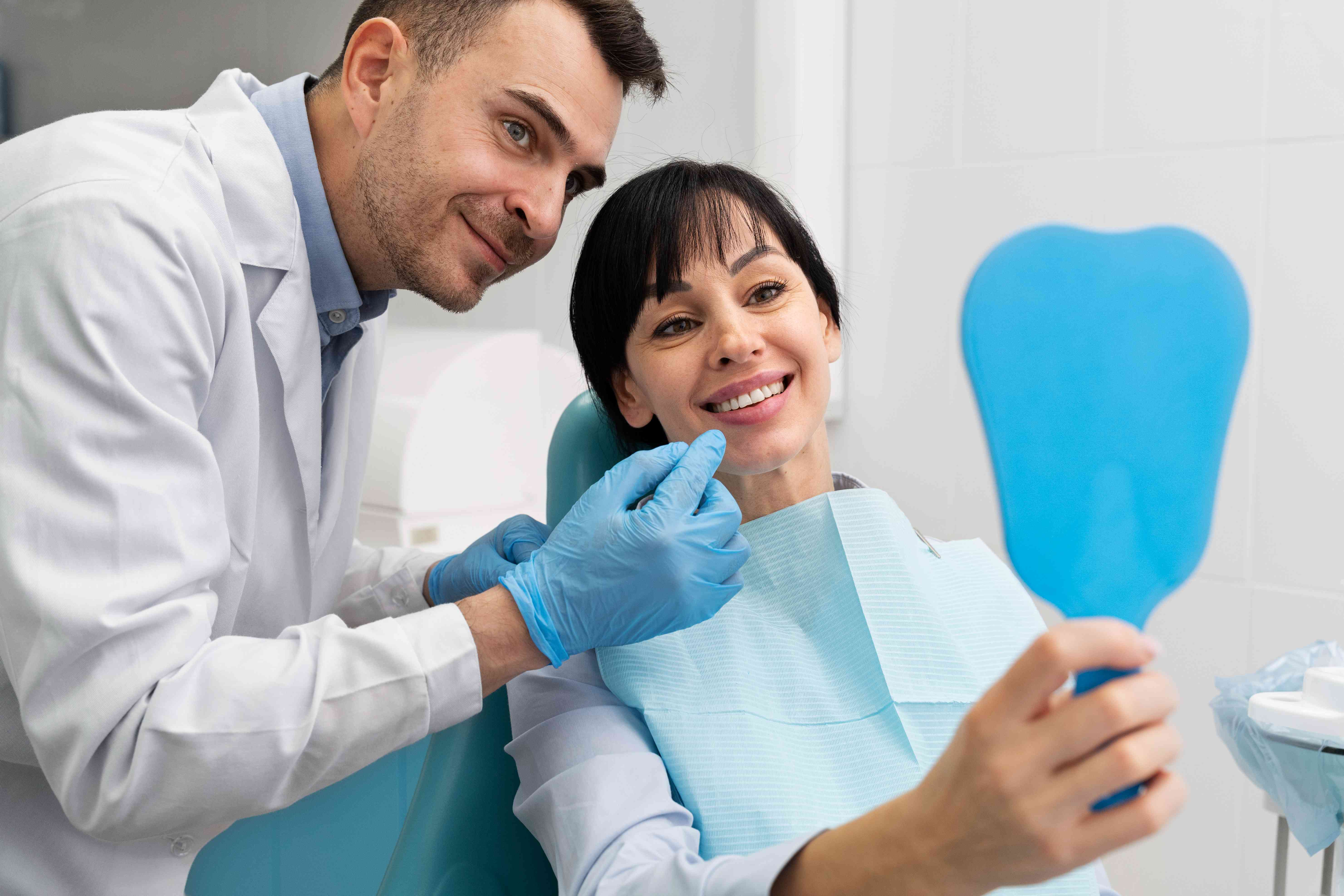 Dentist examining a smiling female patient holding a tooth-shaped mirror.
