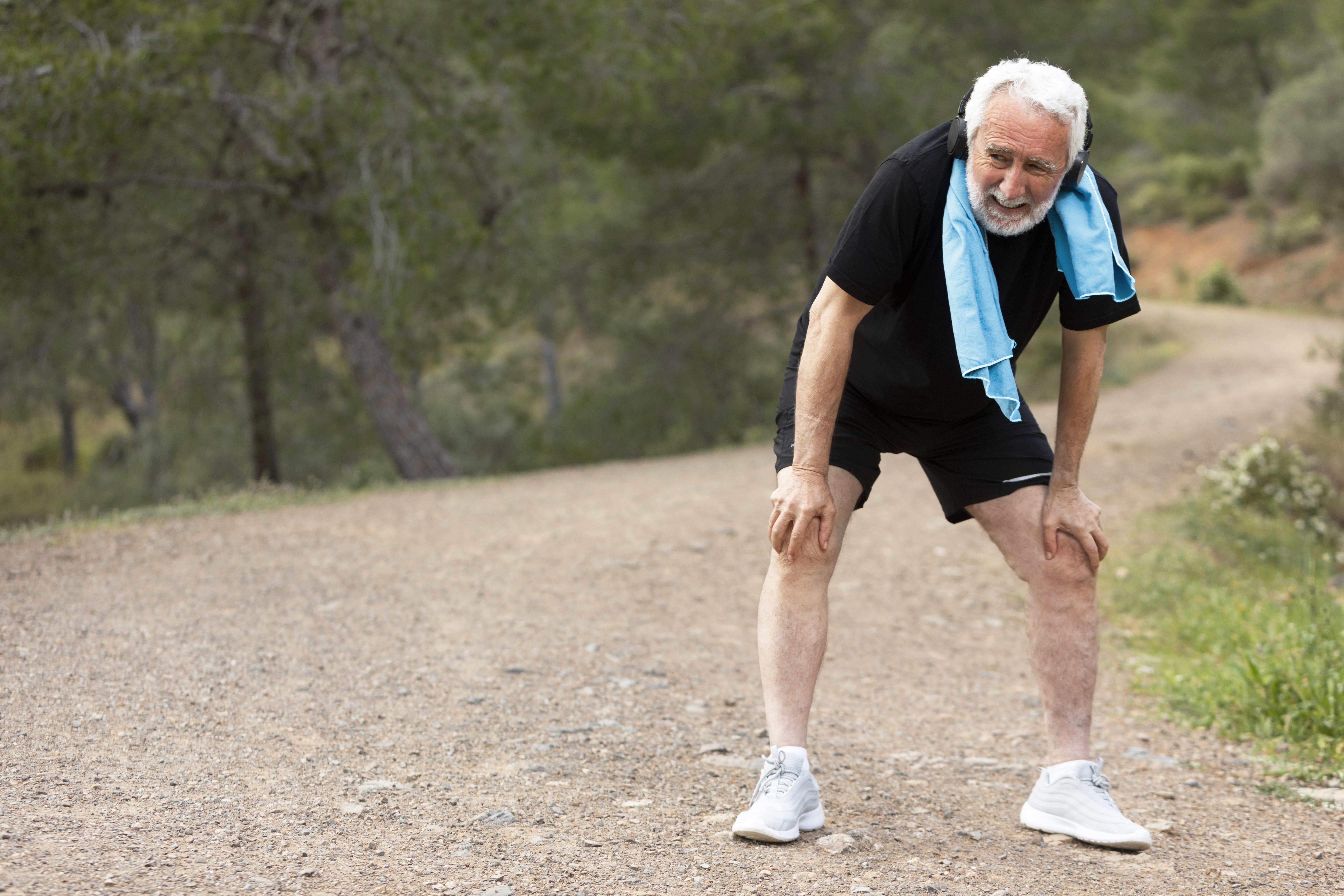 portrait-Close-up of a man in athletic wear holding his knee in apparent discomfort during outdoor activity.senior-man-jogging-mountain
