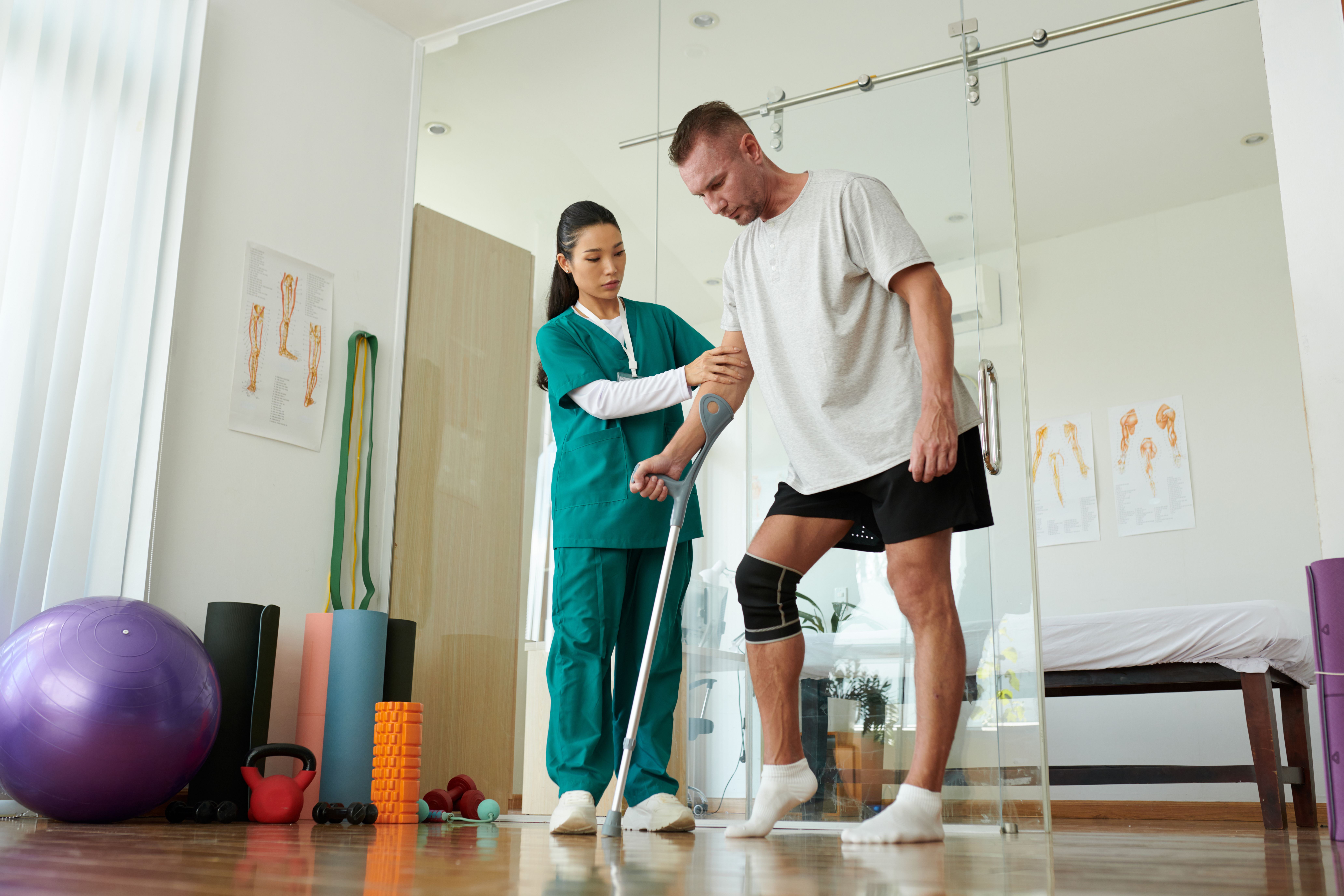 A physiotherapist helping a male patient with a knee brace practice walking using a crutch