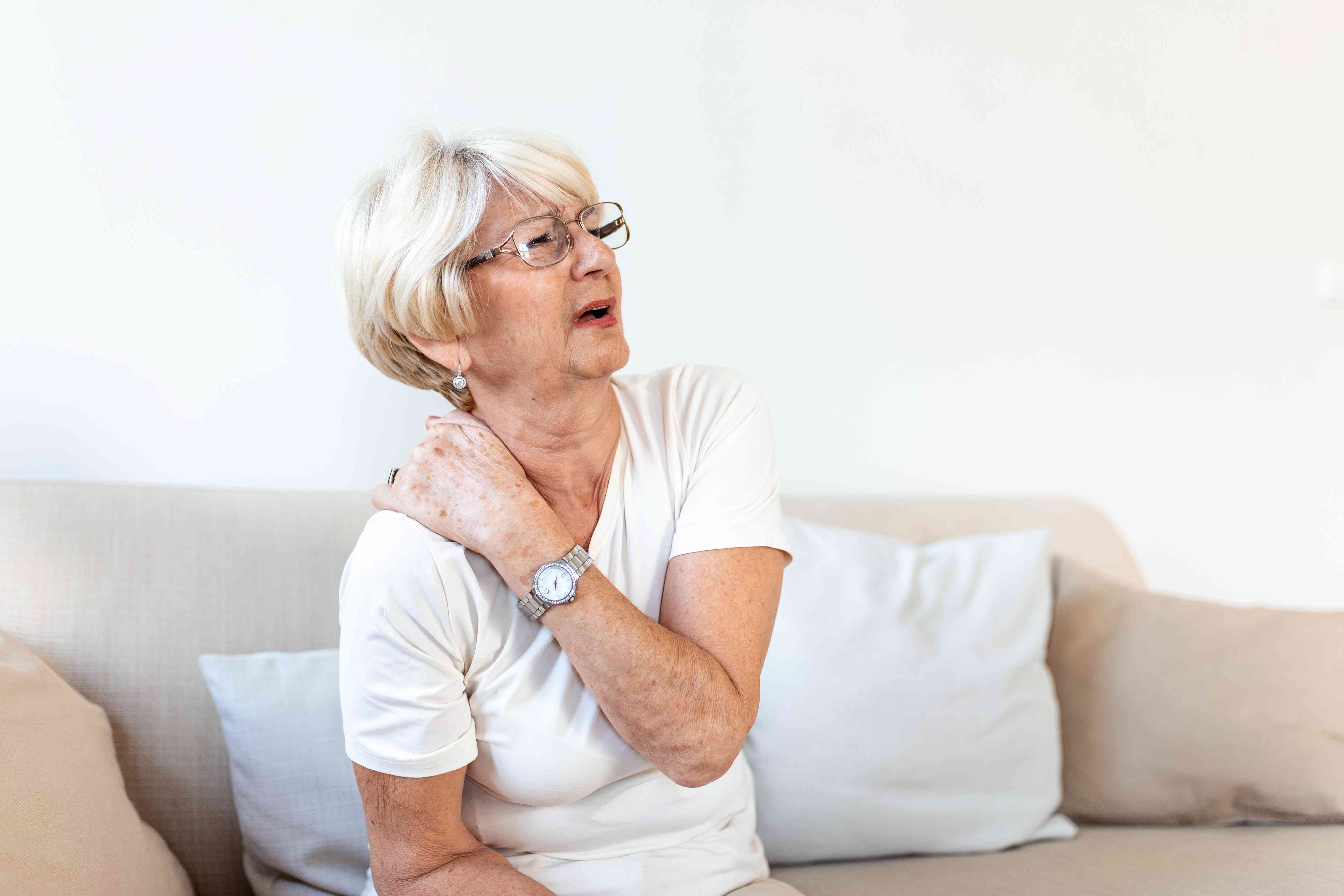 Elderly woman sitting on a couch, holding her shoulder in pain due to bone discomfort
