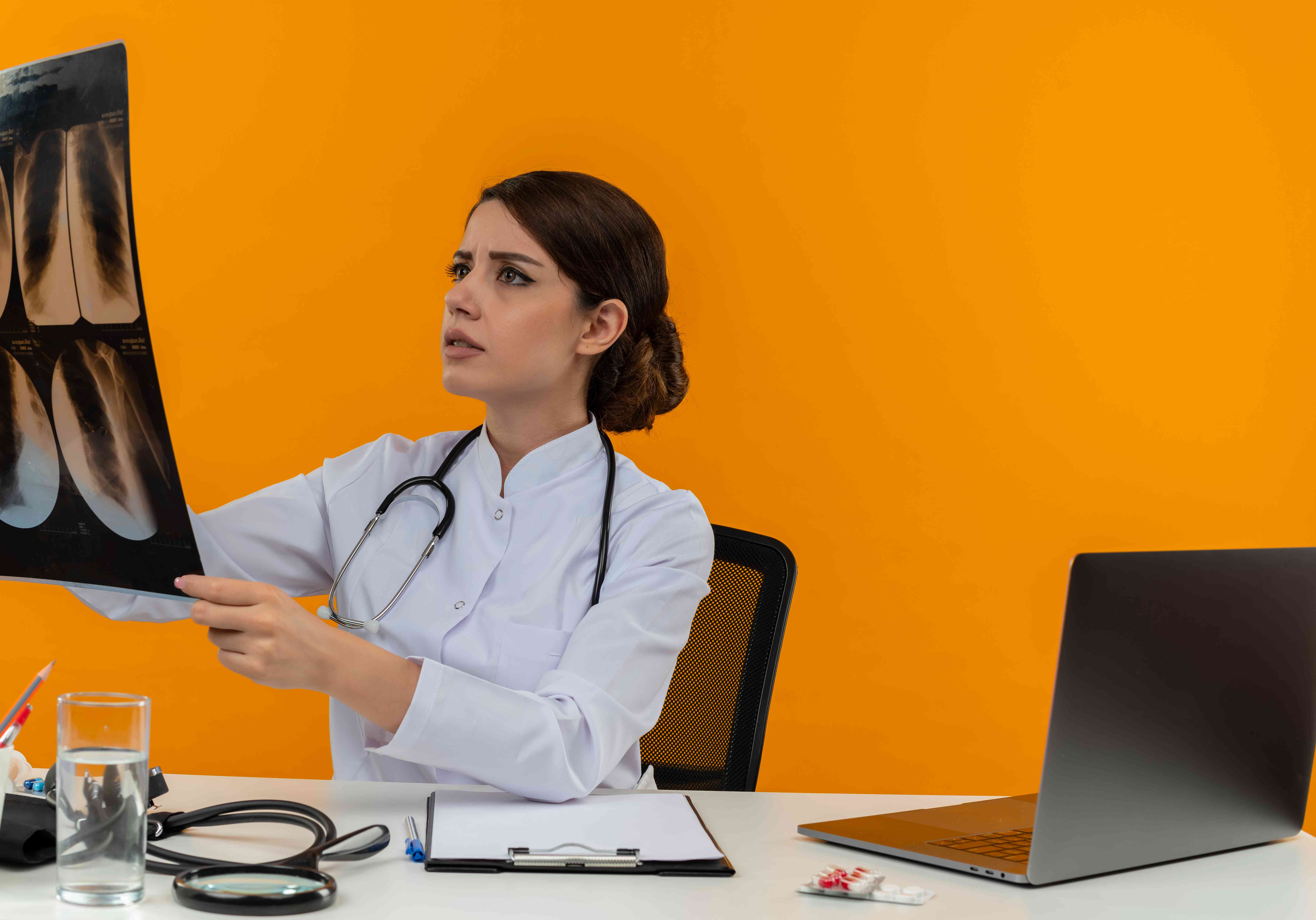 Female doctor examining an X-ray scan while sitting at her desk with a laptop and medical tools