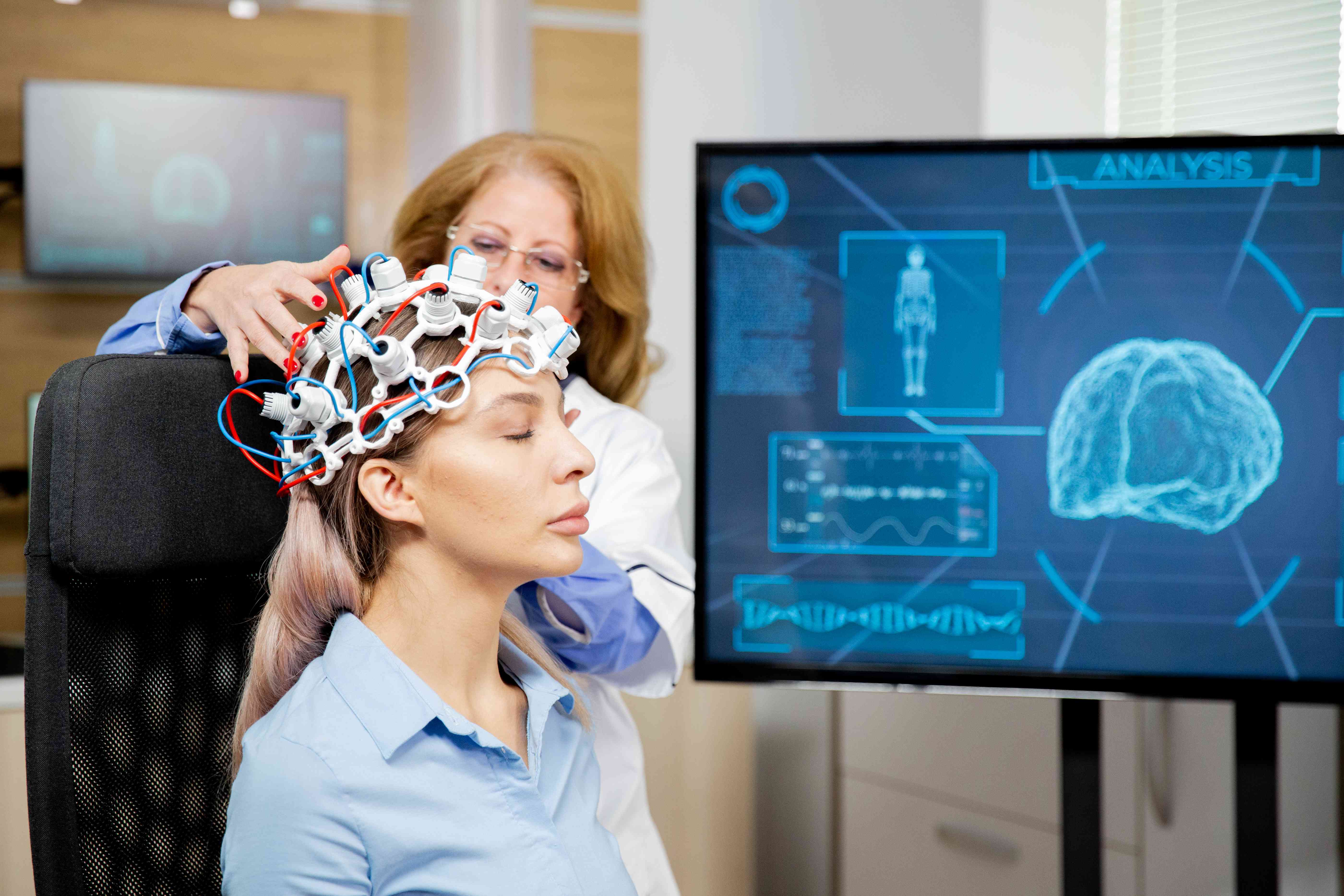 A woman is undergoing a brain scan with a futuristic EEG headset, with digital brain analysis visuals on a screen behind her.