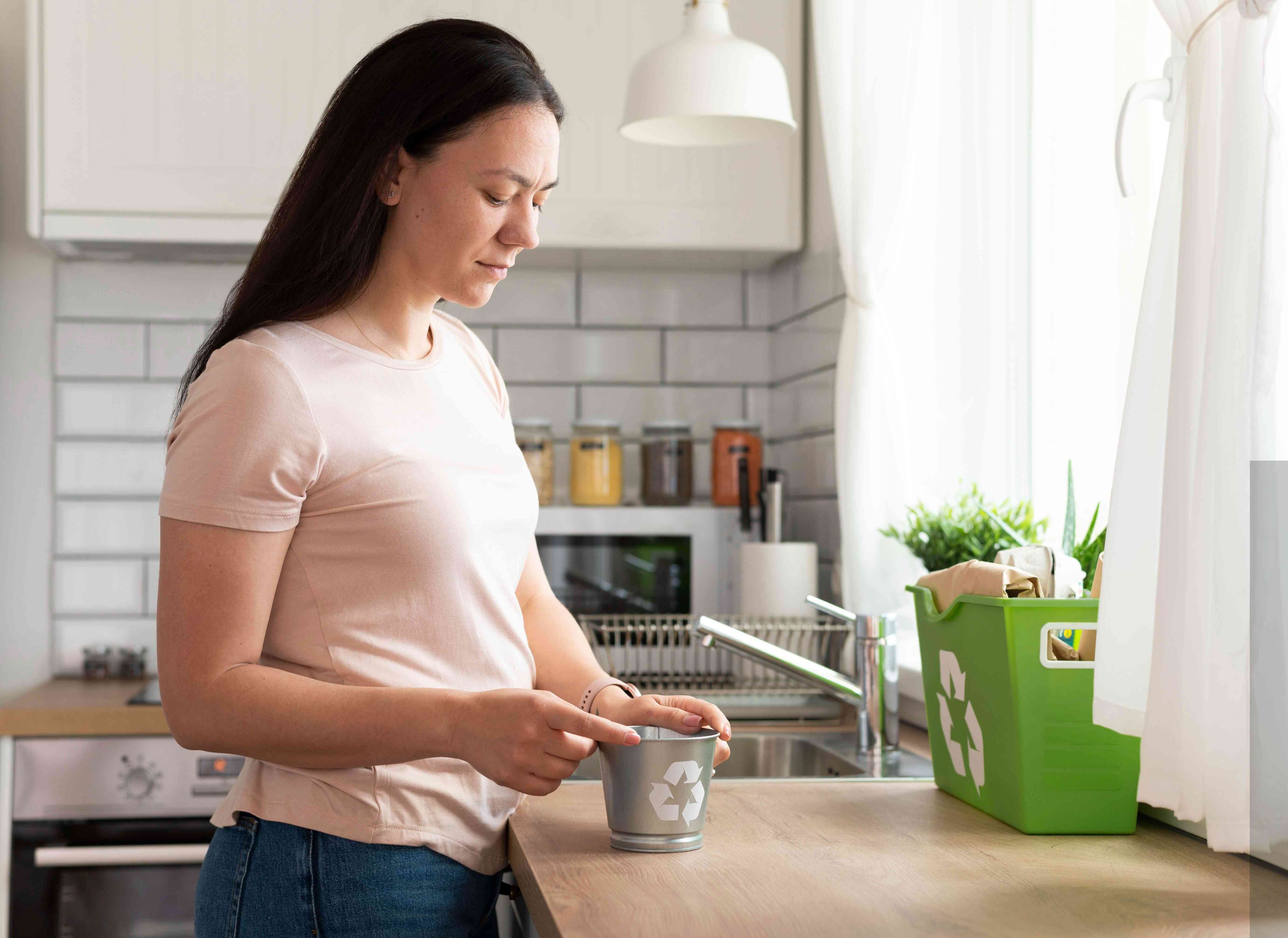 Woman standing in a modern kitchen preparing a herbal or home remedy with eco-friendly containers in the background.