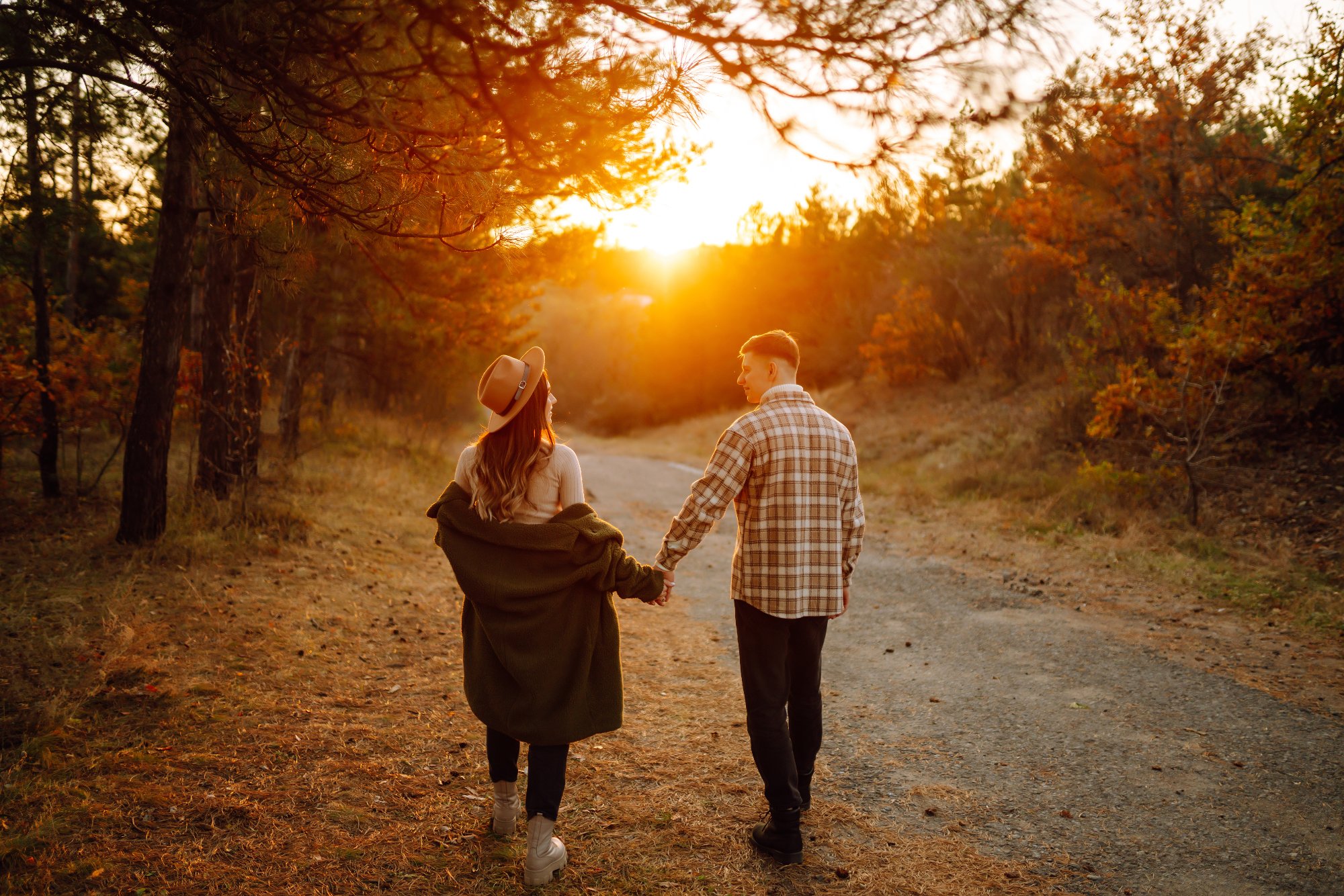 Couple holding hands and walking together down a sunlit autumn path at sunset.