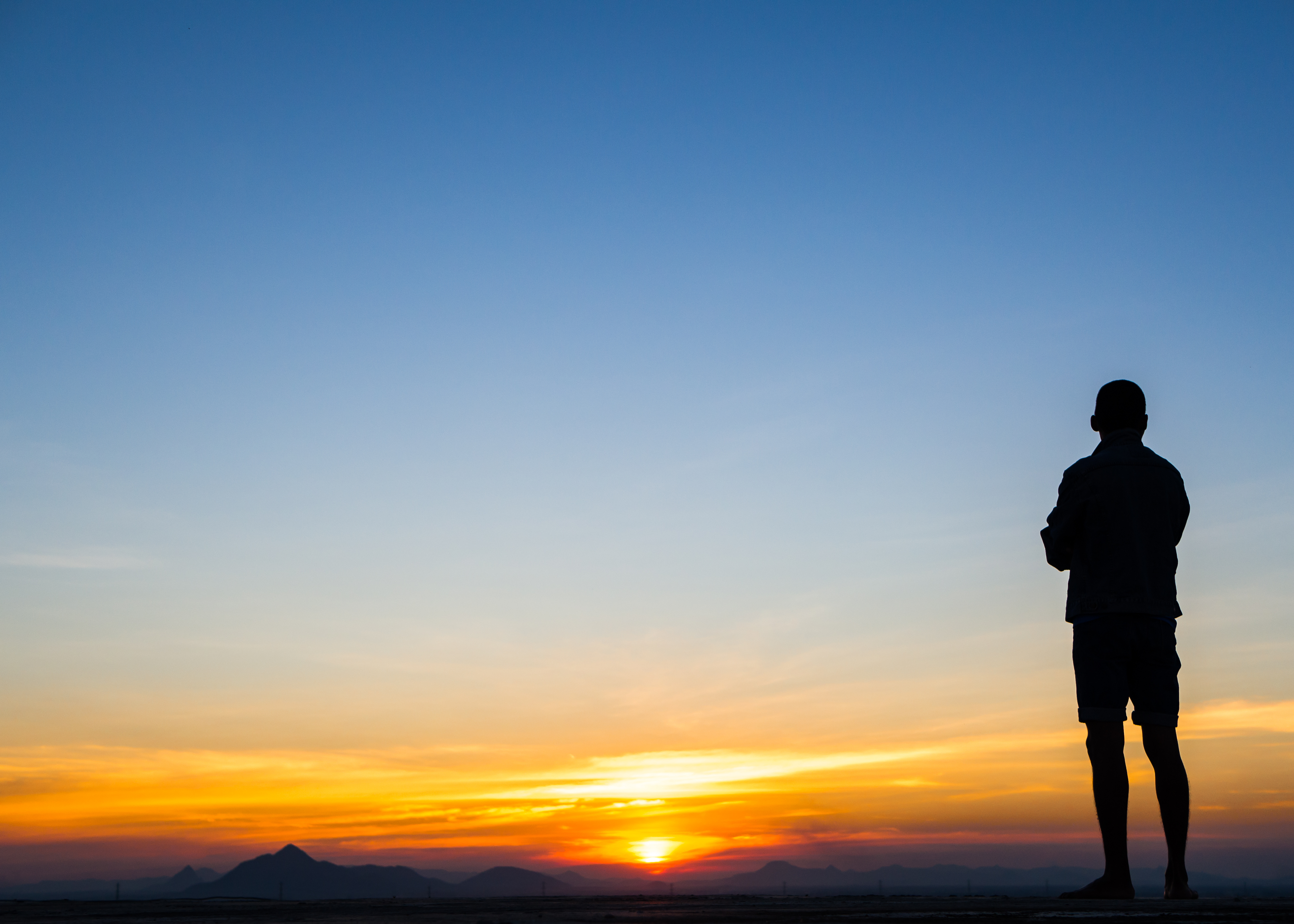 Silhouette of a person standing on a hillside, watching a golden sunrise