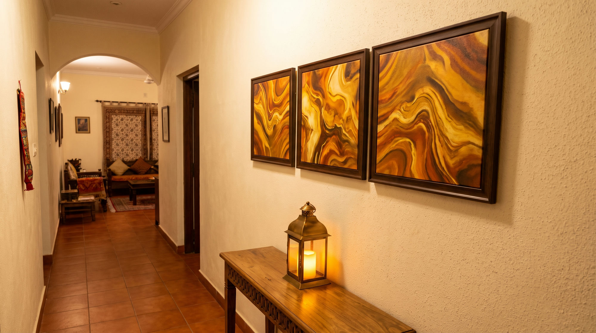Hallway with a triptych of gold and amber abstract canvases and a lit brass lantern on a wooden console