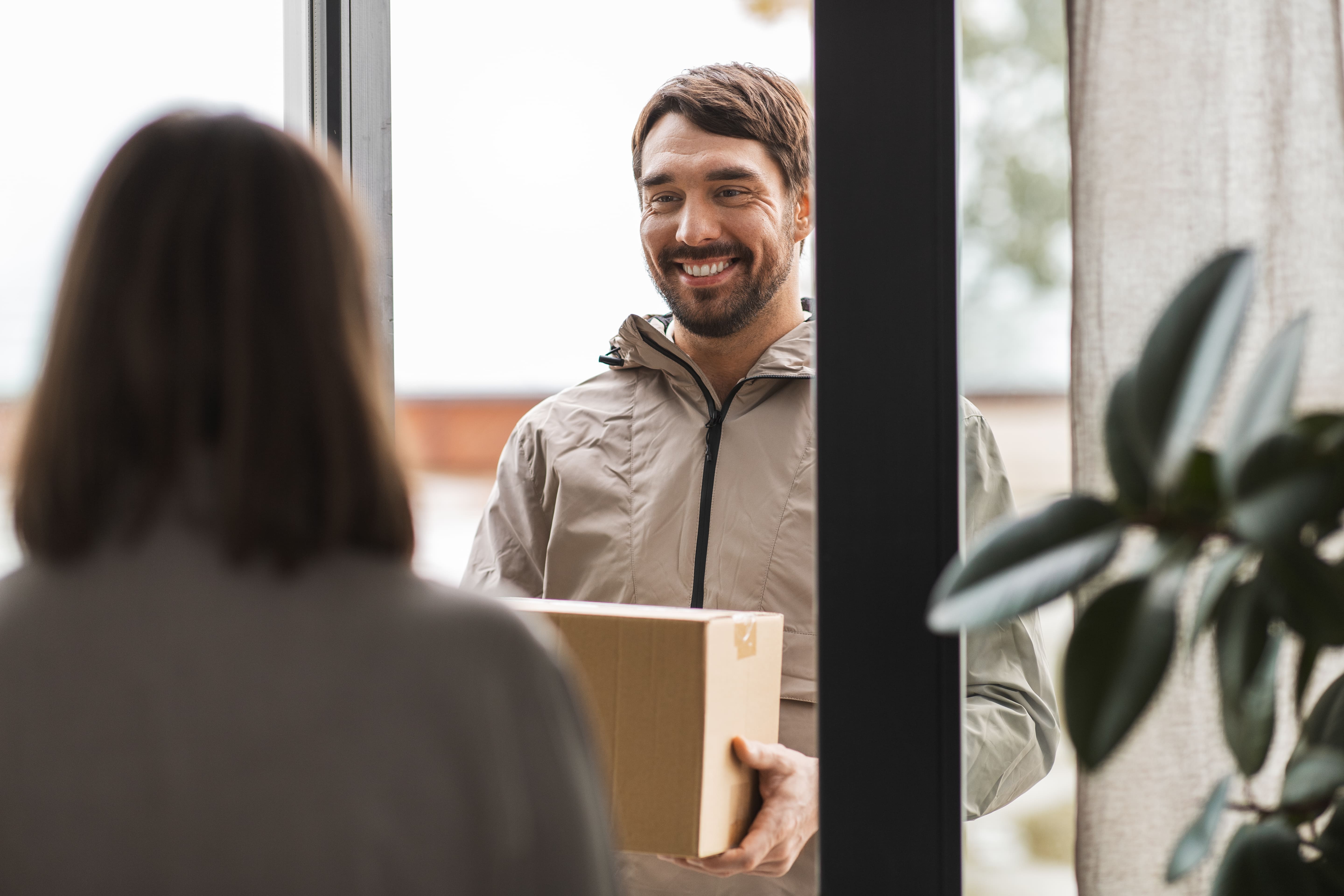 Back profile of a woman standing at her door receiving a package from a happy delivery man.