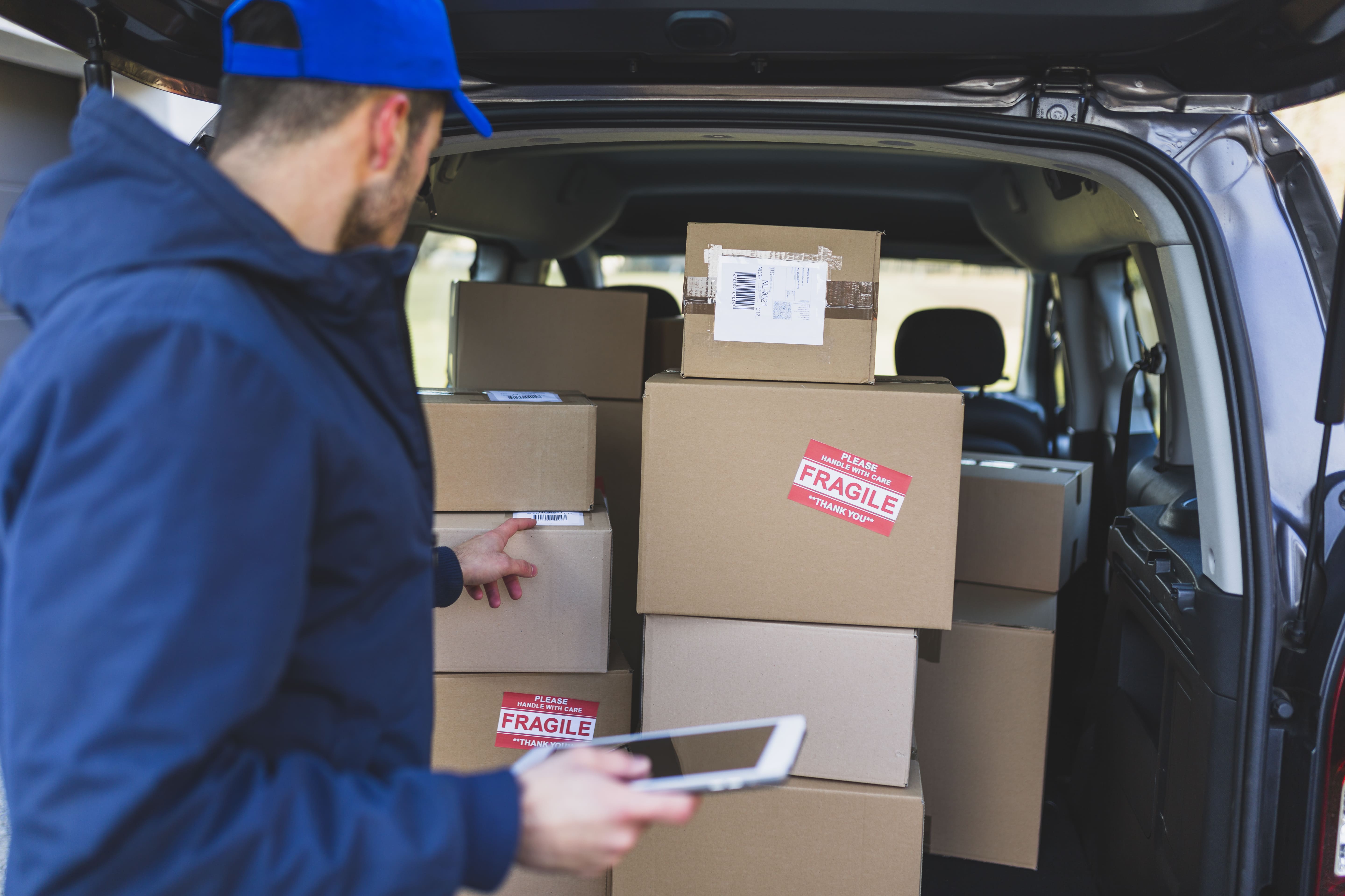 Back profile of delivery man looking at a parcel in the back of a delivery van with a tablet in his hand.