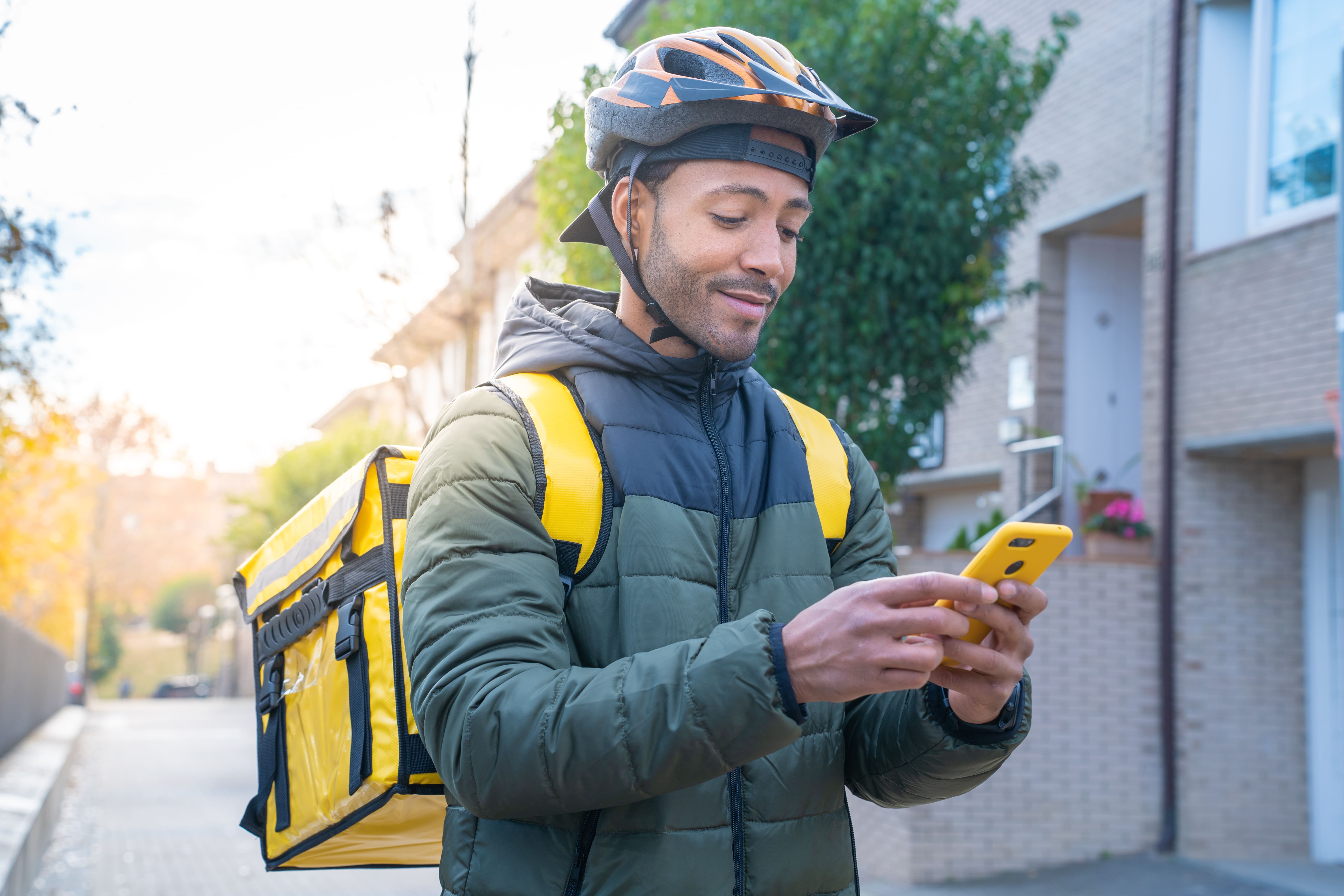 Food delivery man wearing uniform and helmet using mobile device to route him to delivery