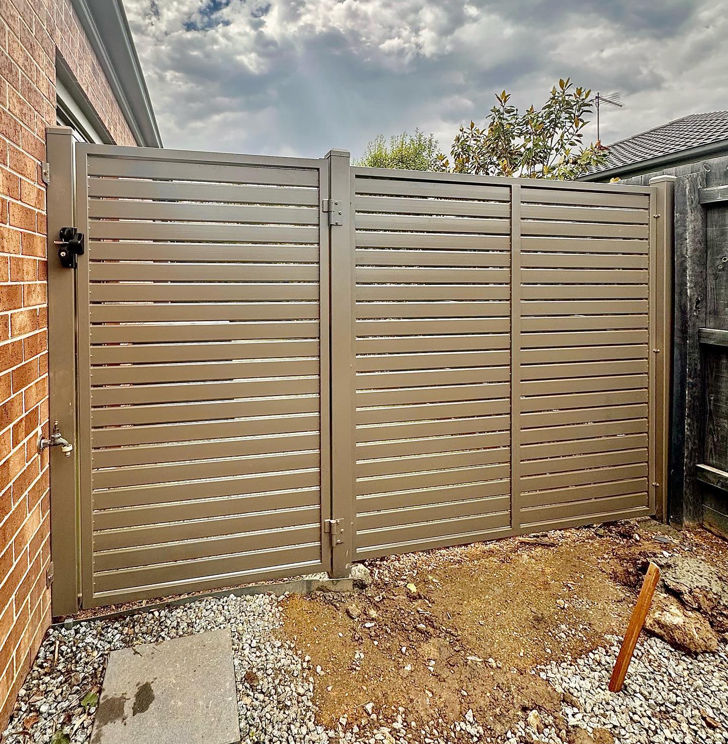 Steel slat fencing between brick wall and wooden fence