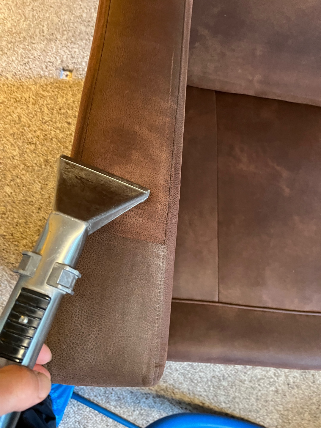 Close-up view of cleaning tool used on brown couch arm