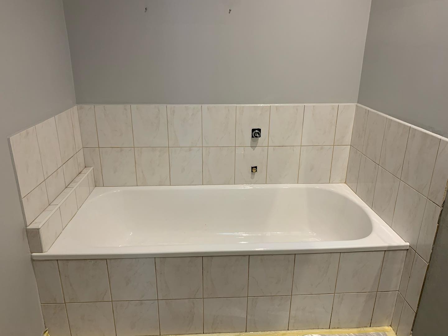 Bathtub surrounded by white tiles with subtle marble pattern during renovation