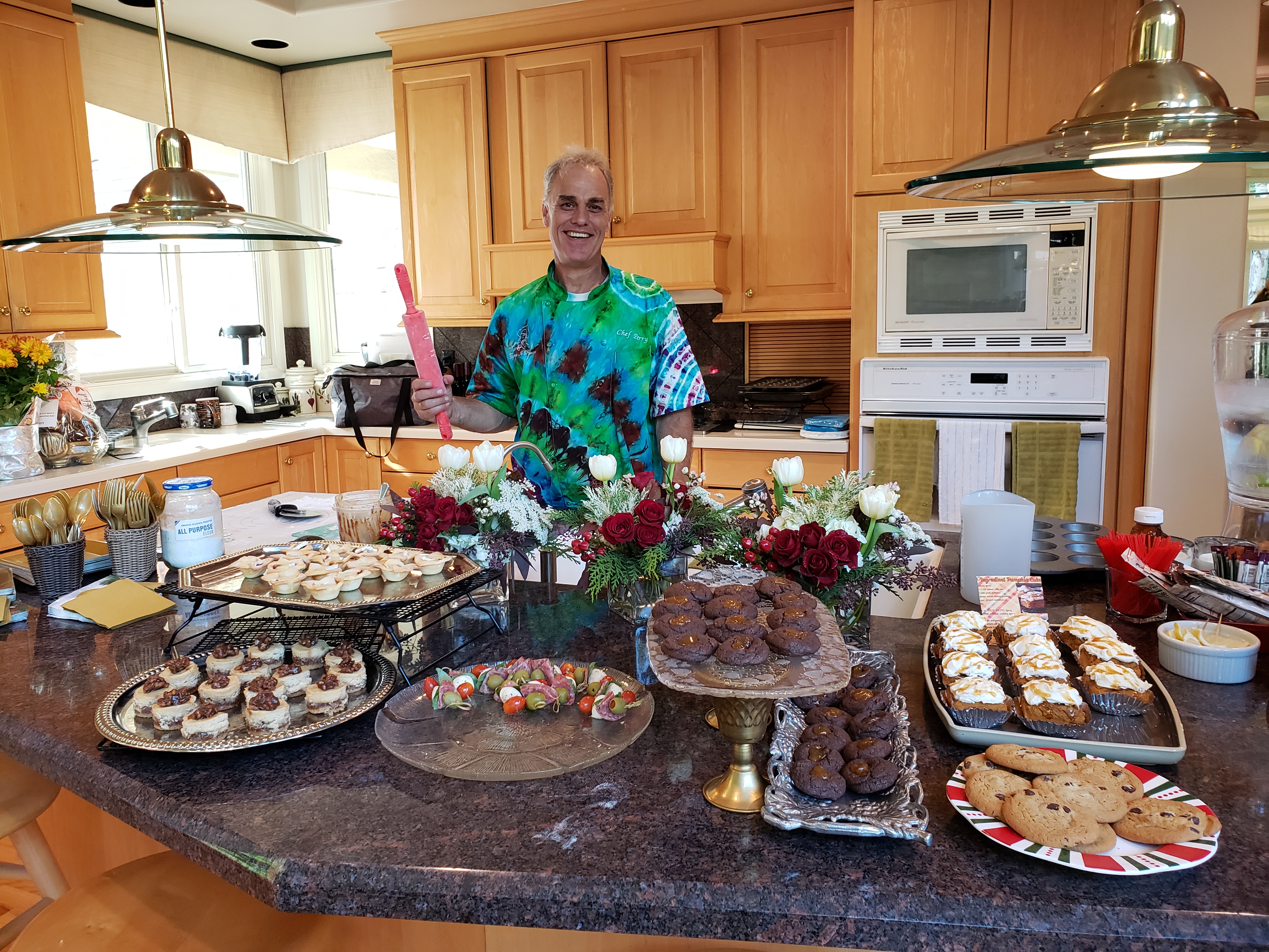 Chef Perry smiling behind a kitchen island filled with desserts