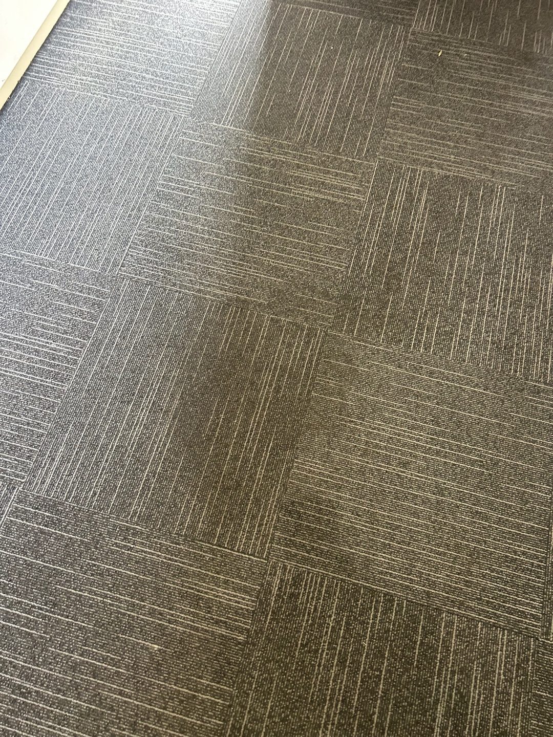 A section of commercial carpet tiles showing varying shades of grey after cleaning