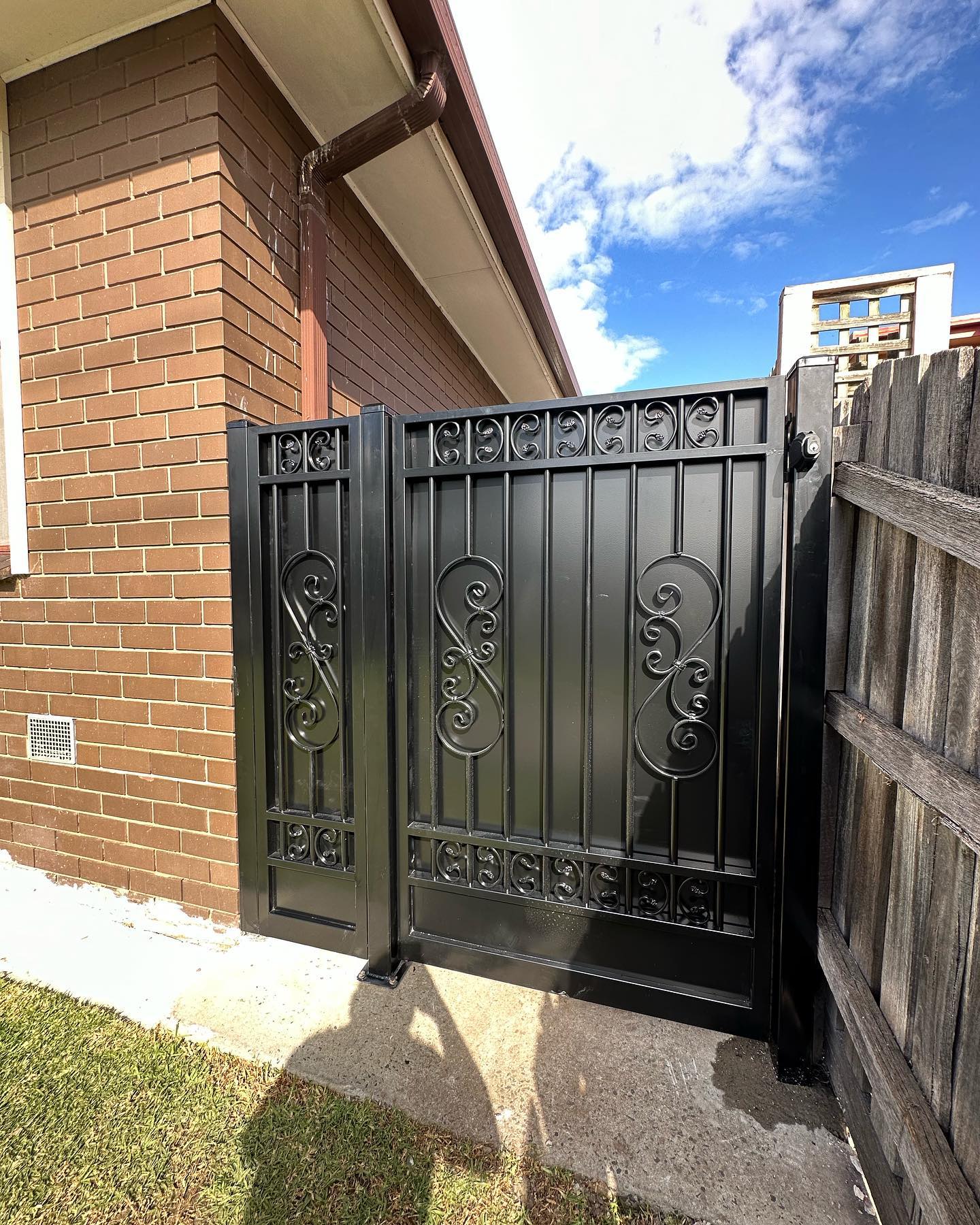 Decorative black pedestrian gates installed between brick wall and wooden fence