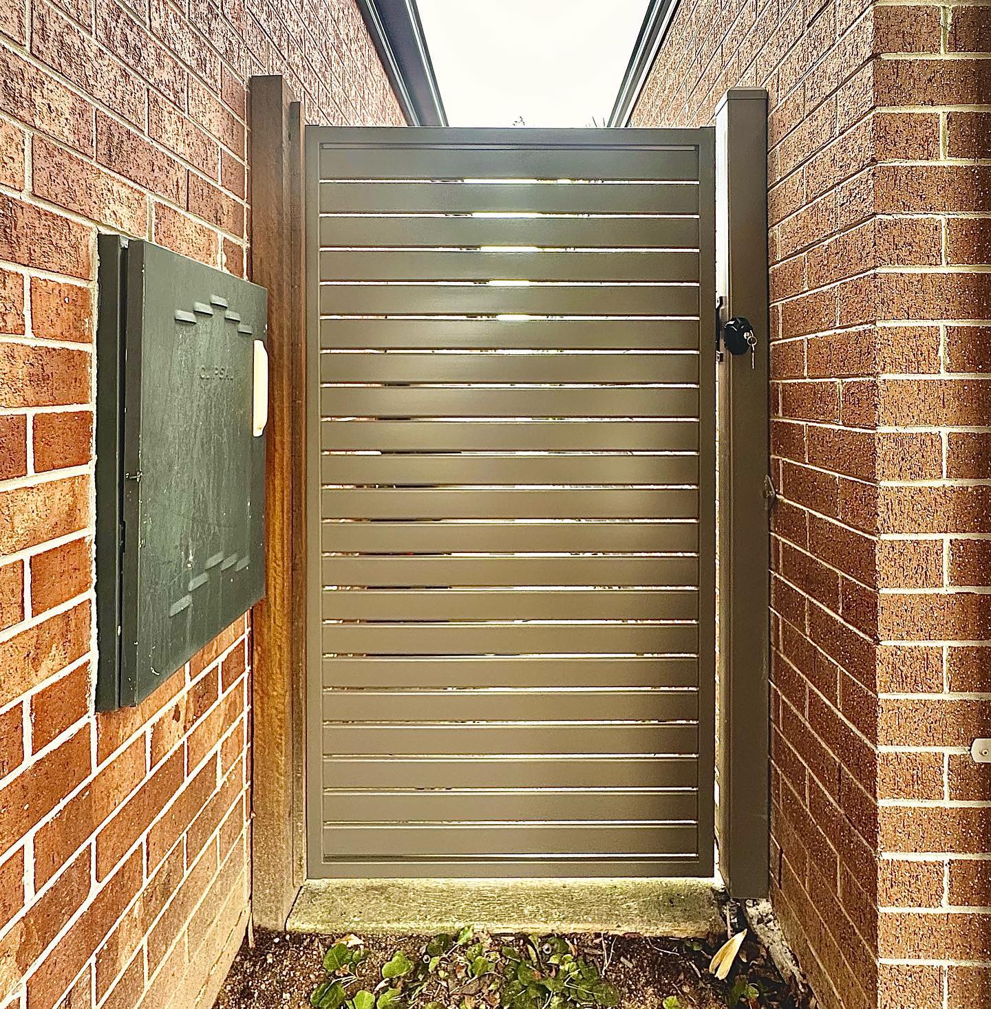 Horizontal steel slat gate between brick walls