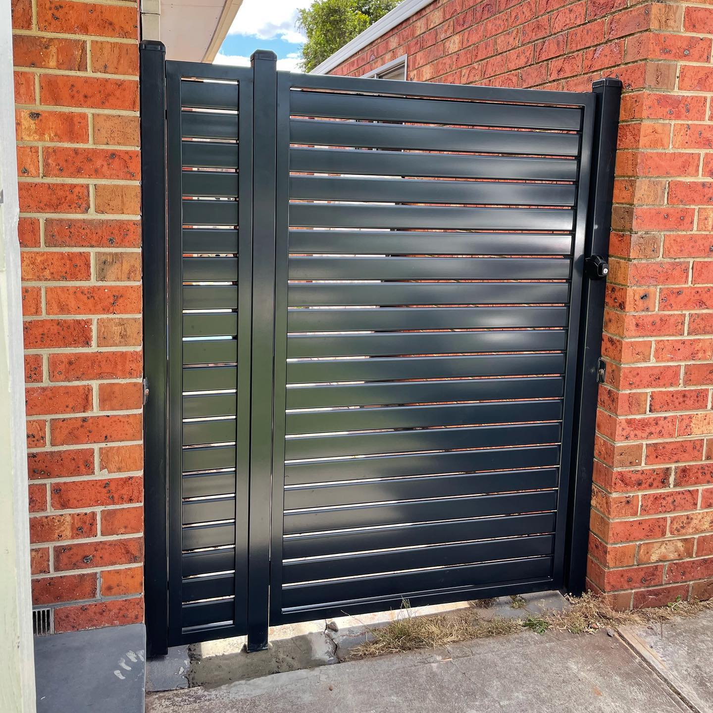Black slat fencing gate installed between two red brick walls