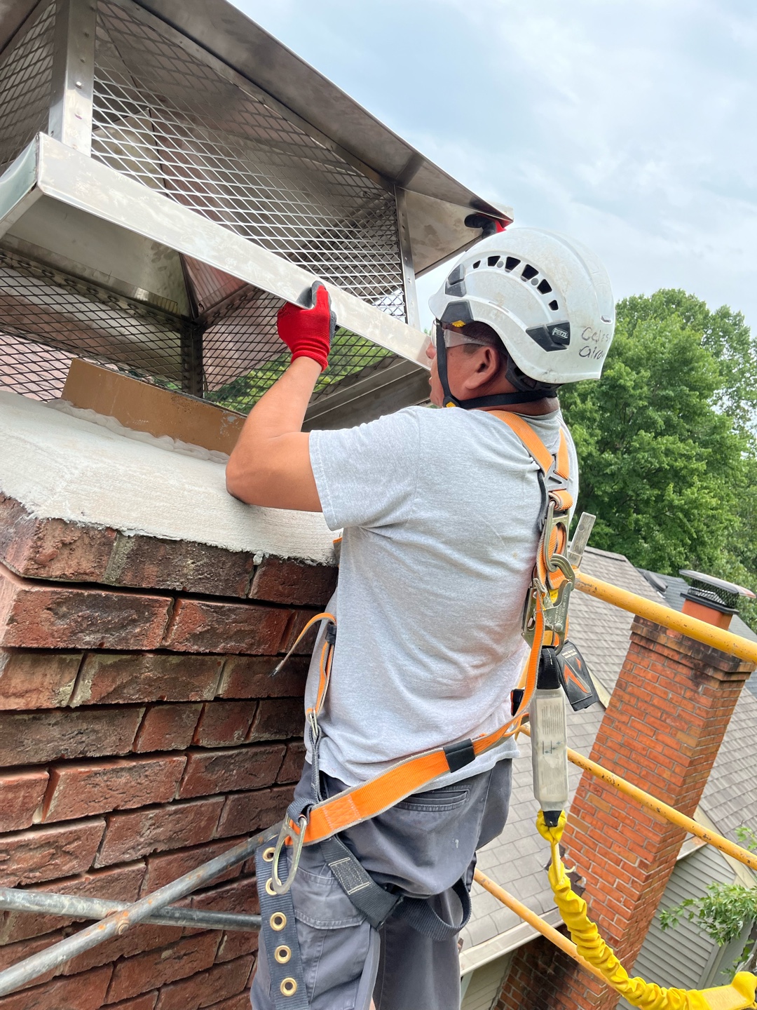 Worker installing metal mount cap on brick chimney