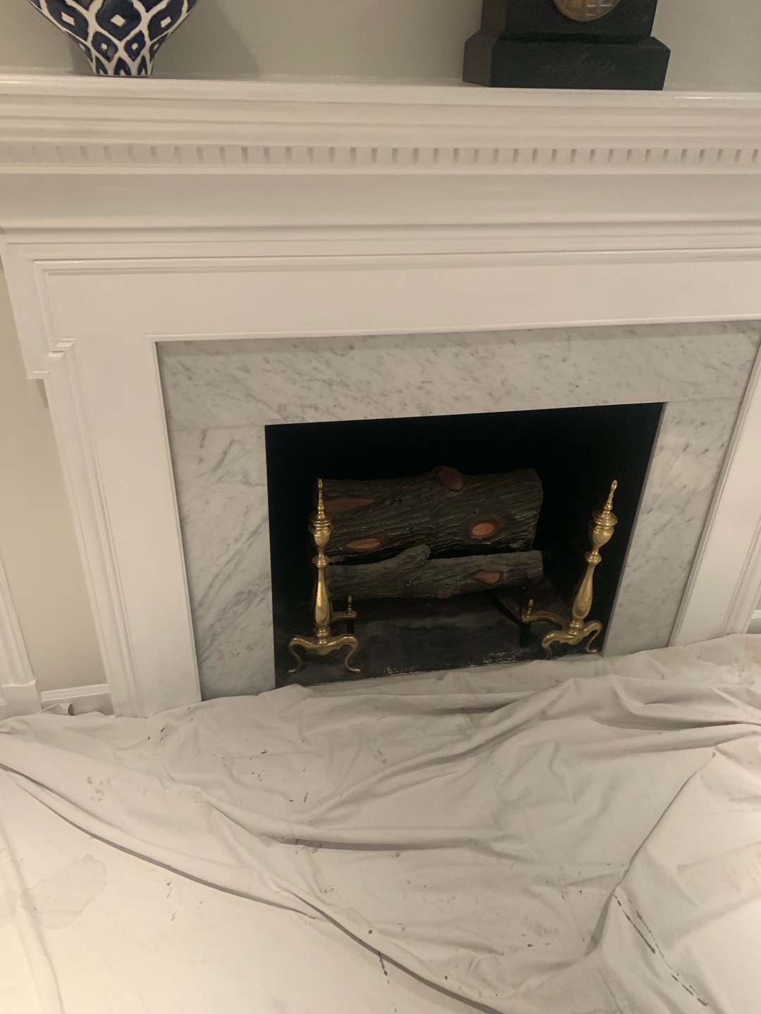 A white marble fireplace with intricate molding before renovation