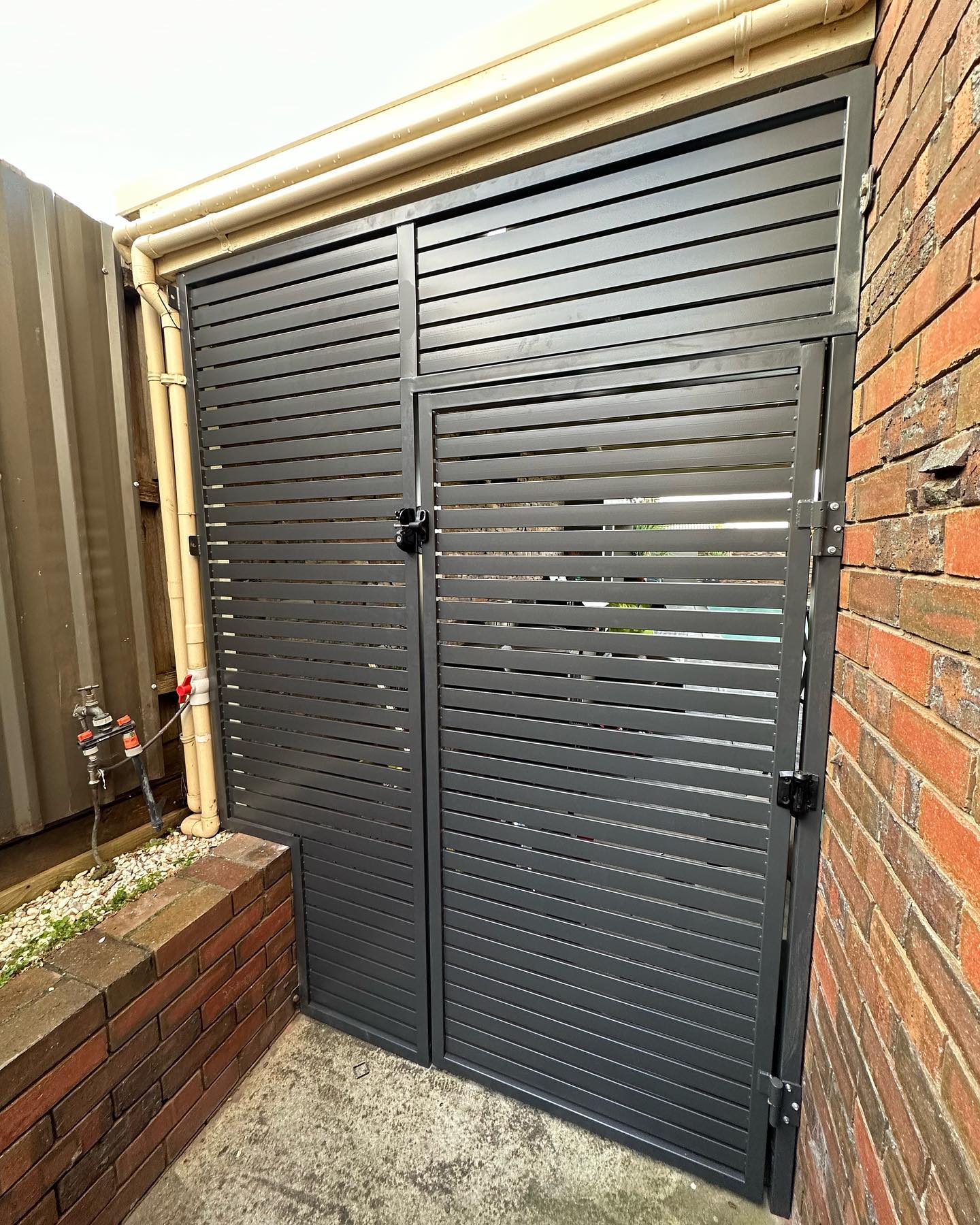 Custom slat gate installed between brick wall and metal structure