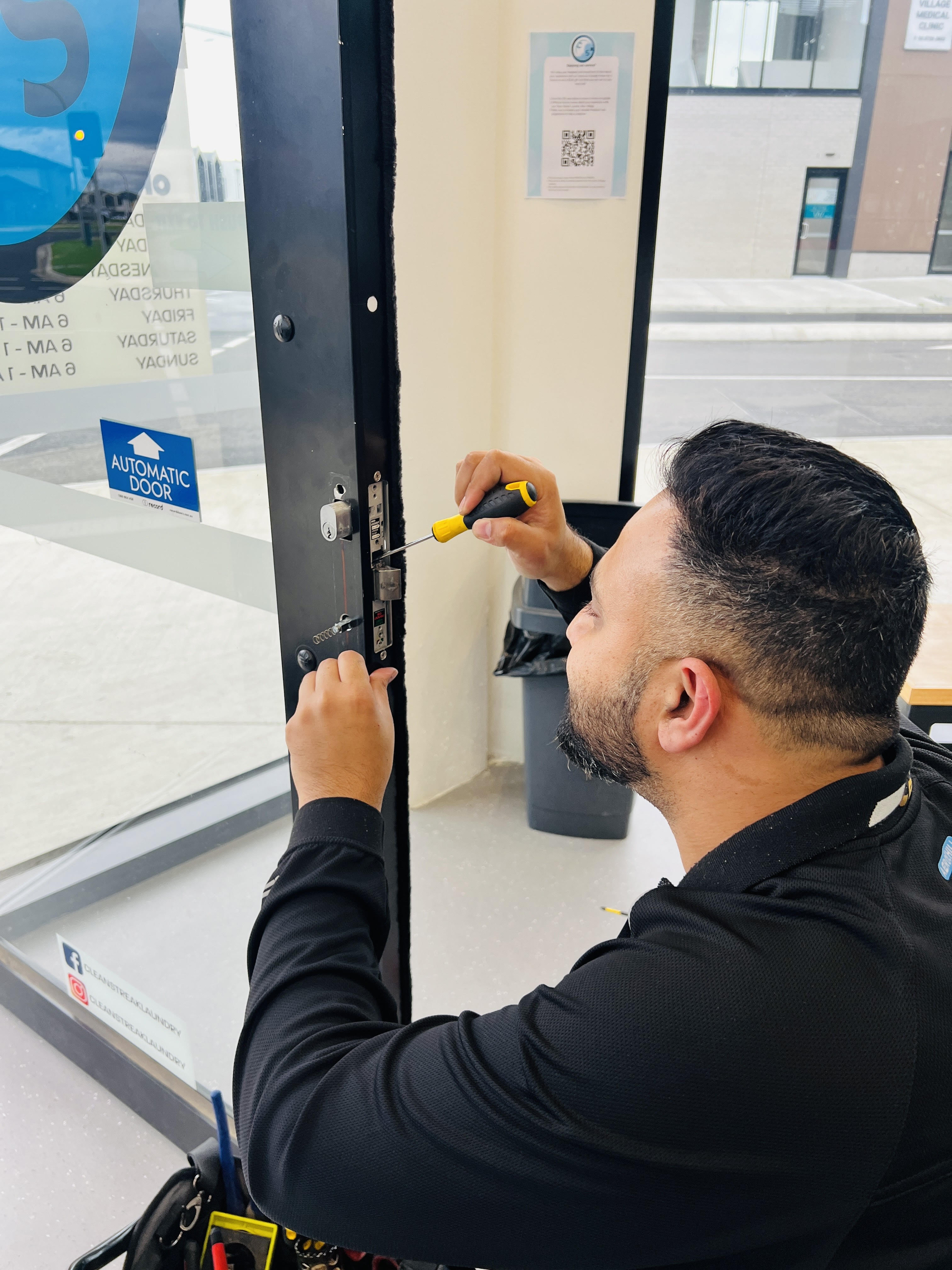 A professional locksmith installing a new lock on a glass door at a commercial location