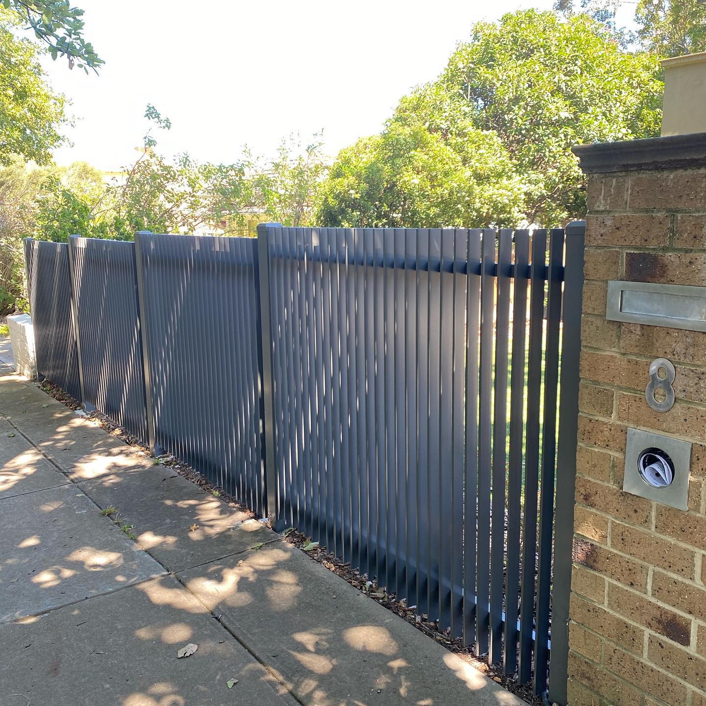 Modern residential fence made of vertical metal slats painted in dark color