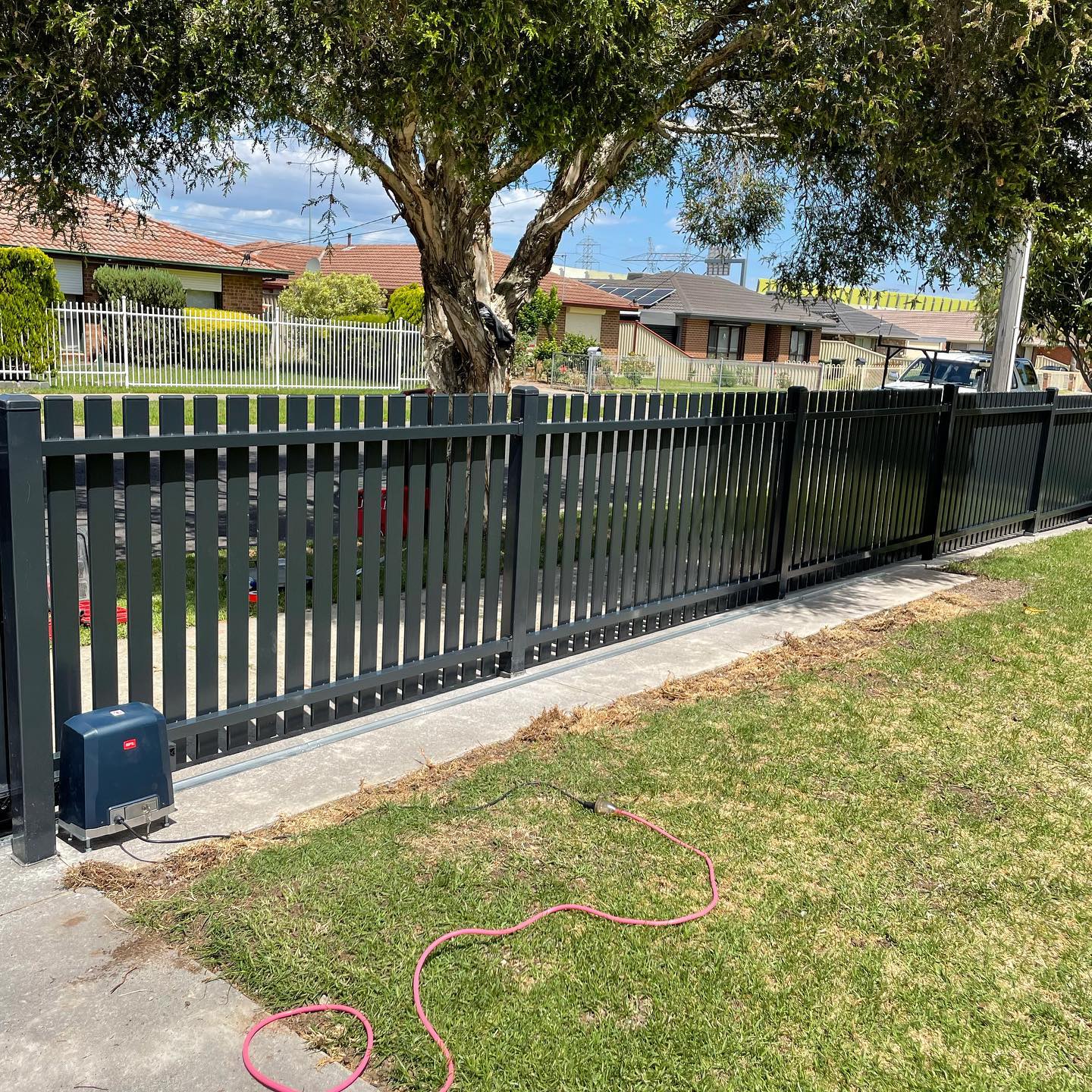 Black metal fence along property edge with automated gate motor